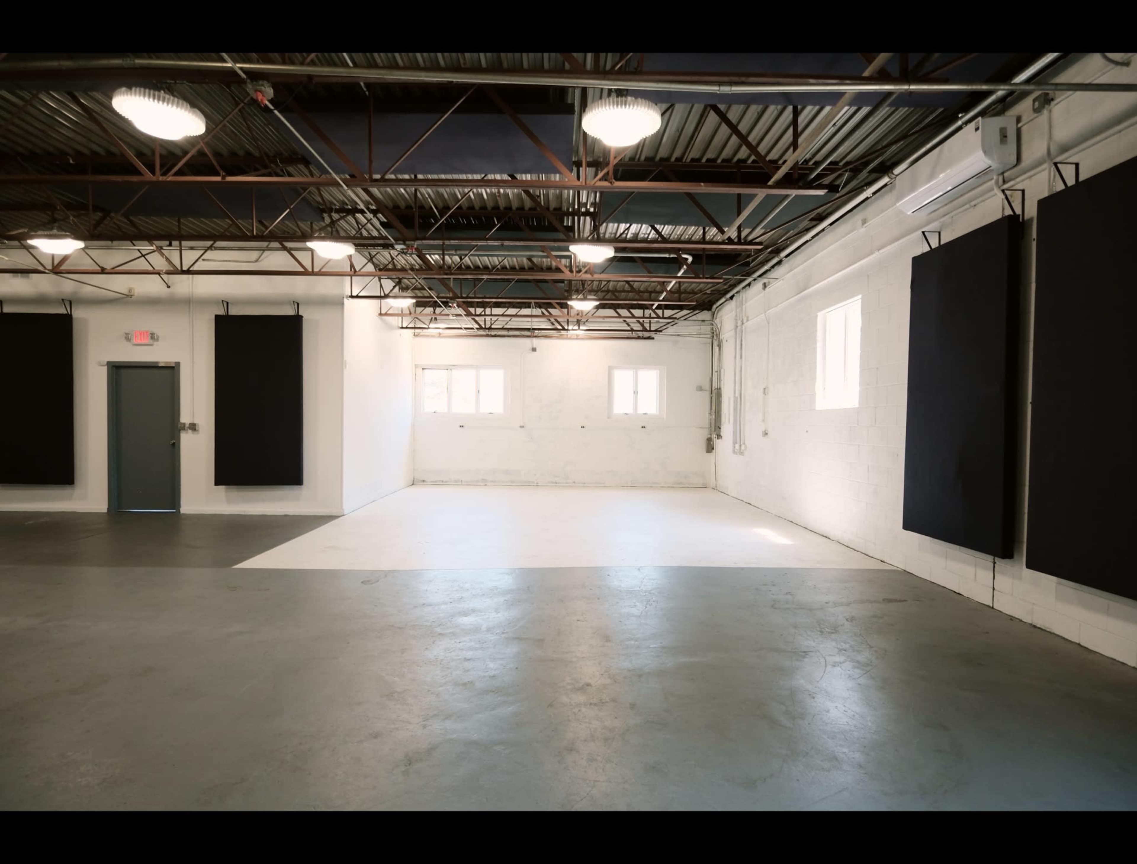The image shows a spacious, empty industrial room with concrete floors and large black panels hanging on the walls.