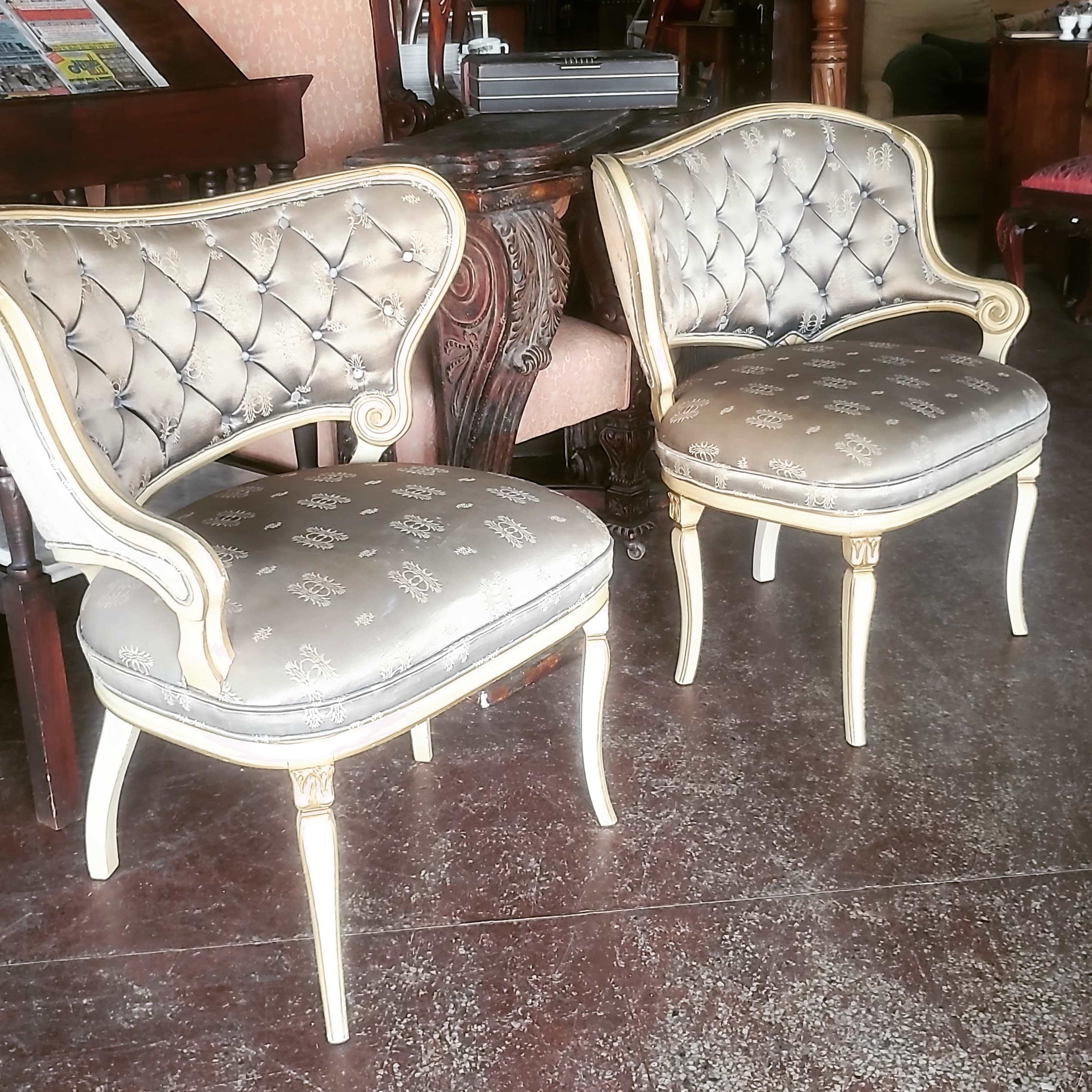 Two upholstered chairs with decorative, tufted backs and carved wooden legs are positioned in a room with wooden furniture.