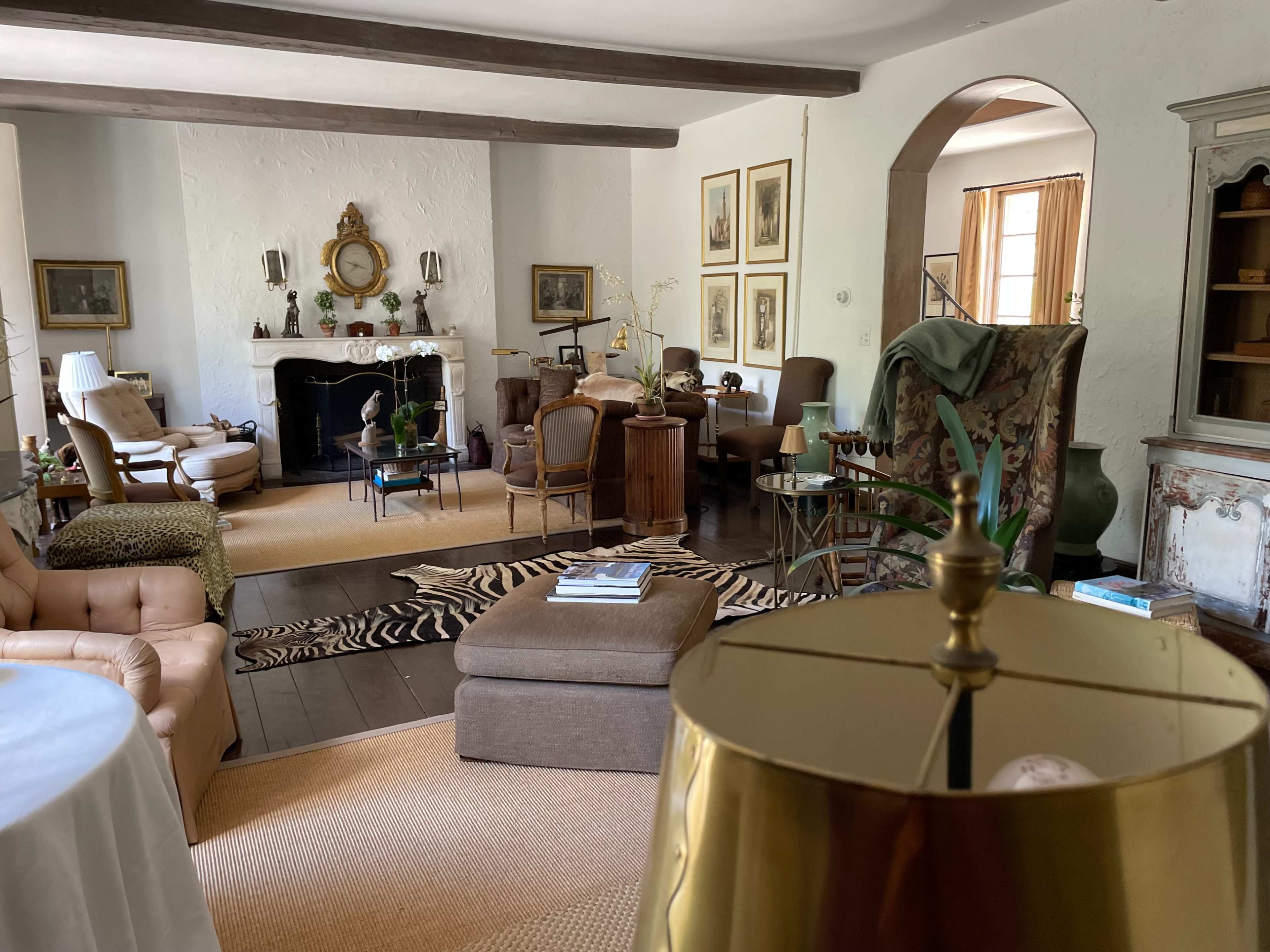 The image shows a spacious living room featuring a mix of vintage furniture, an ornate fireplace, and a range of decorative art pieces.