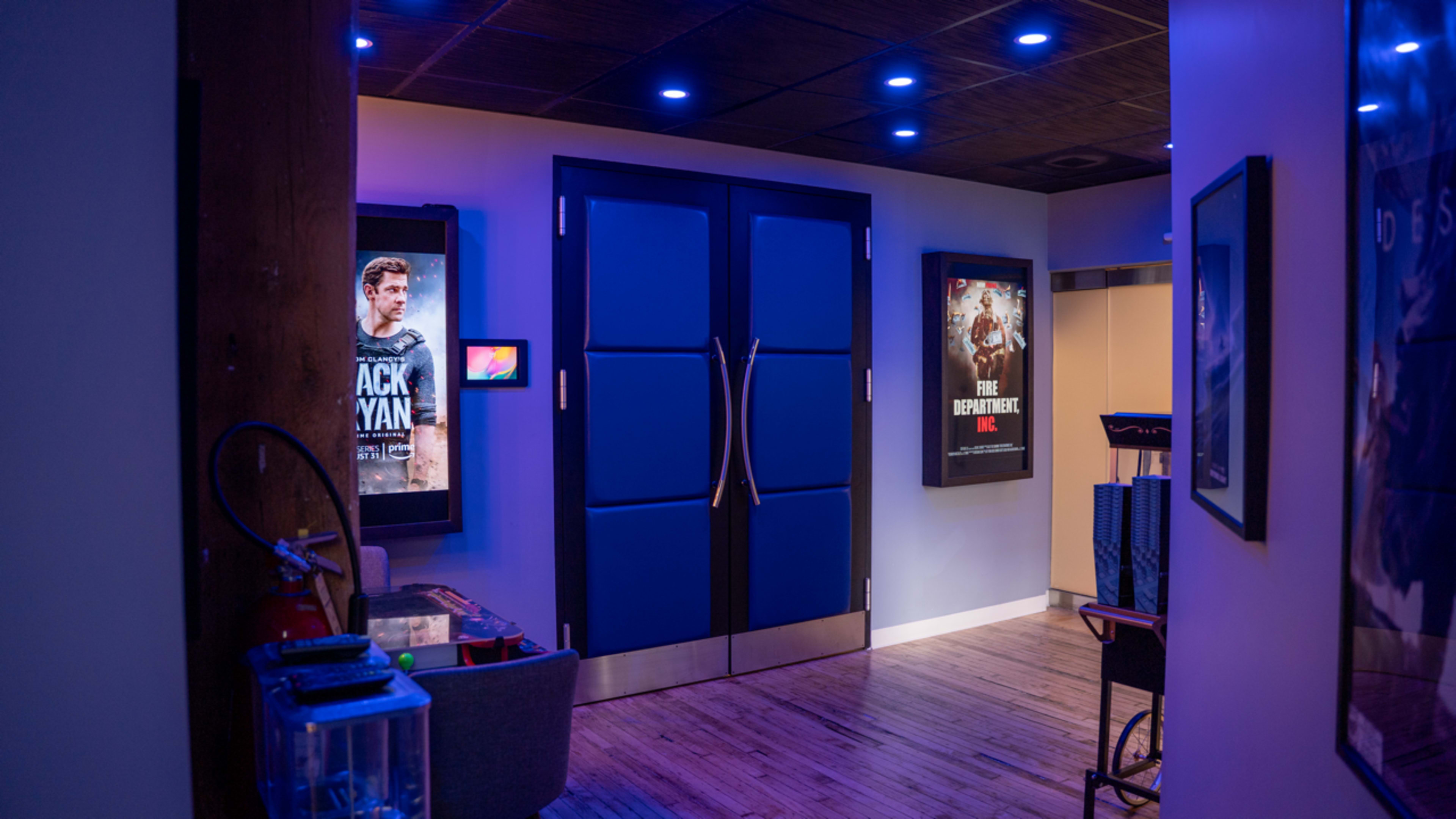 The image shows a modern hallway with blue walls, featuring movie posters on either side and a pair of double doors at the end.