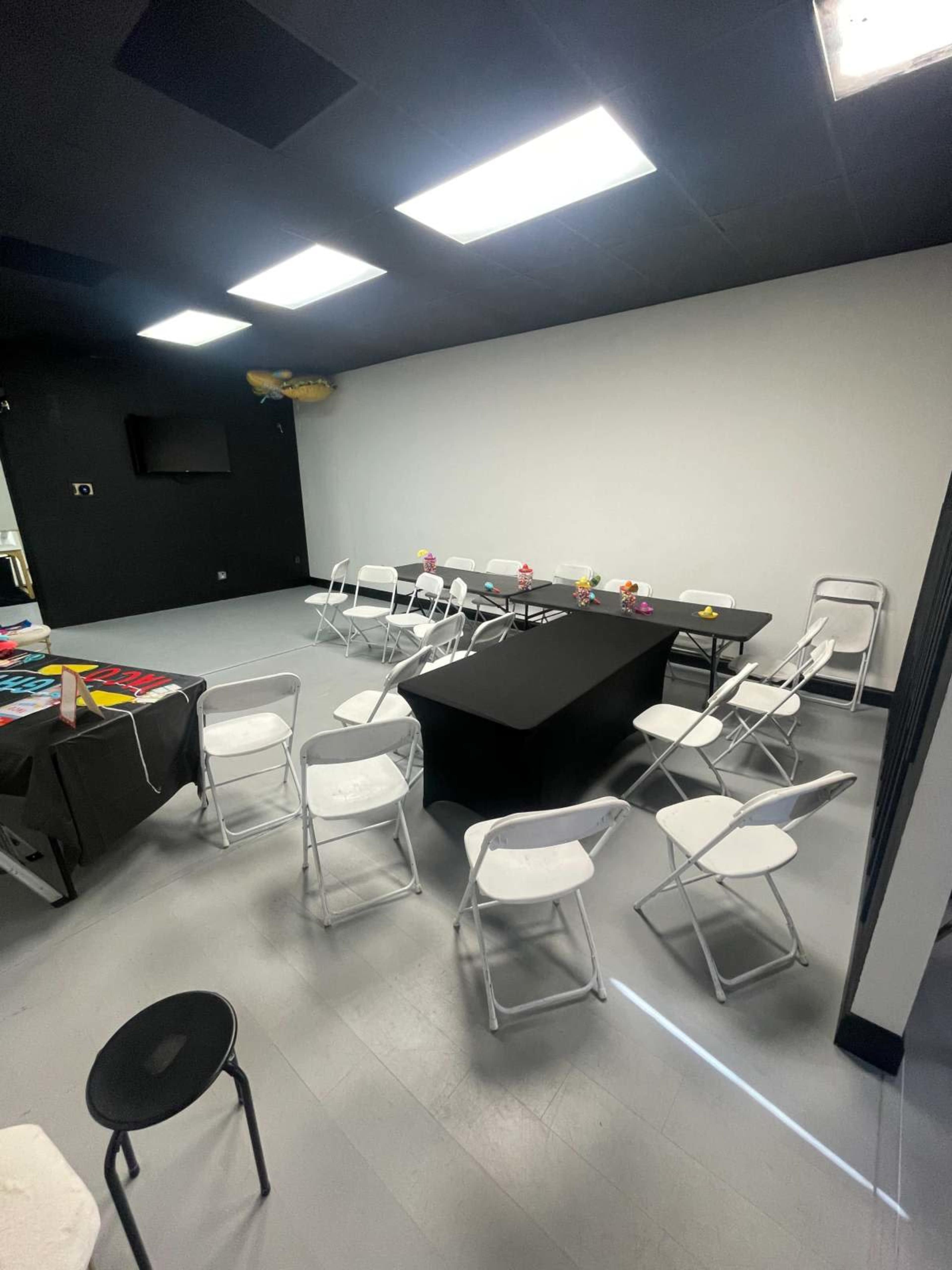 The image shows a spacious, well-lit room set up for a meeting, featuring a long table surrounded by folding chairs and decorative items on the table.