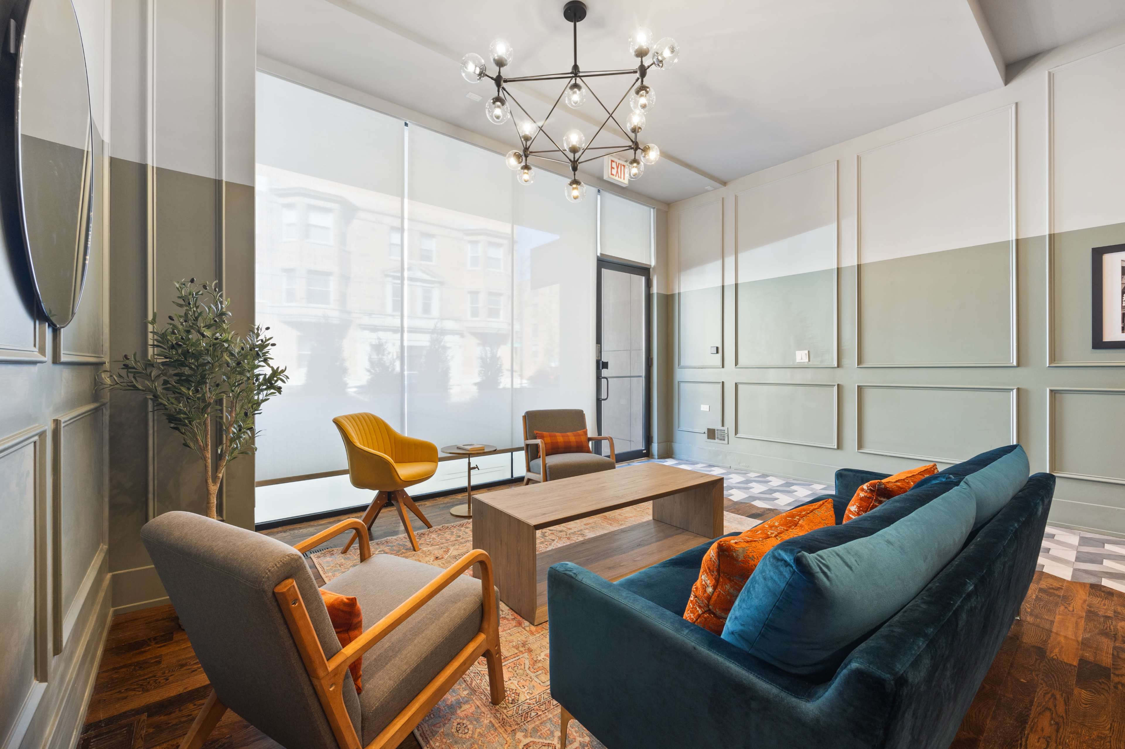The scene features a modern lounge area with a green and white color scheme, a stylish chandelier, and a mix of seating options including a teal sofa and yellow armchairs.