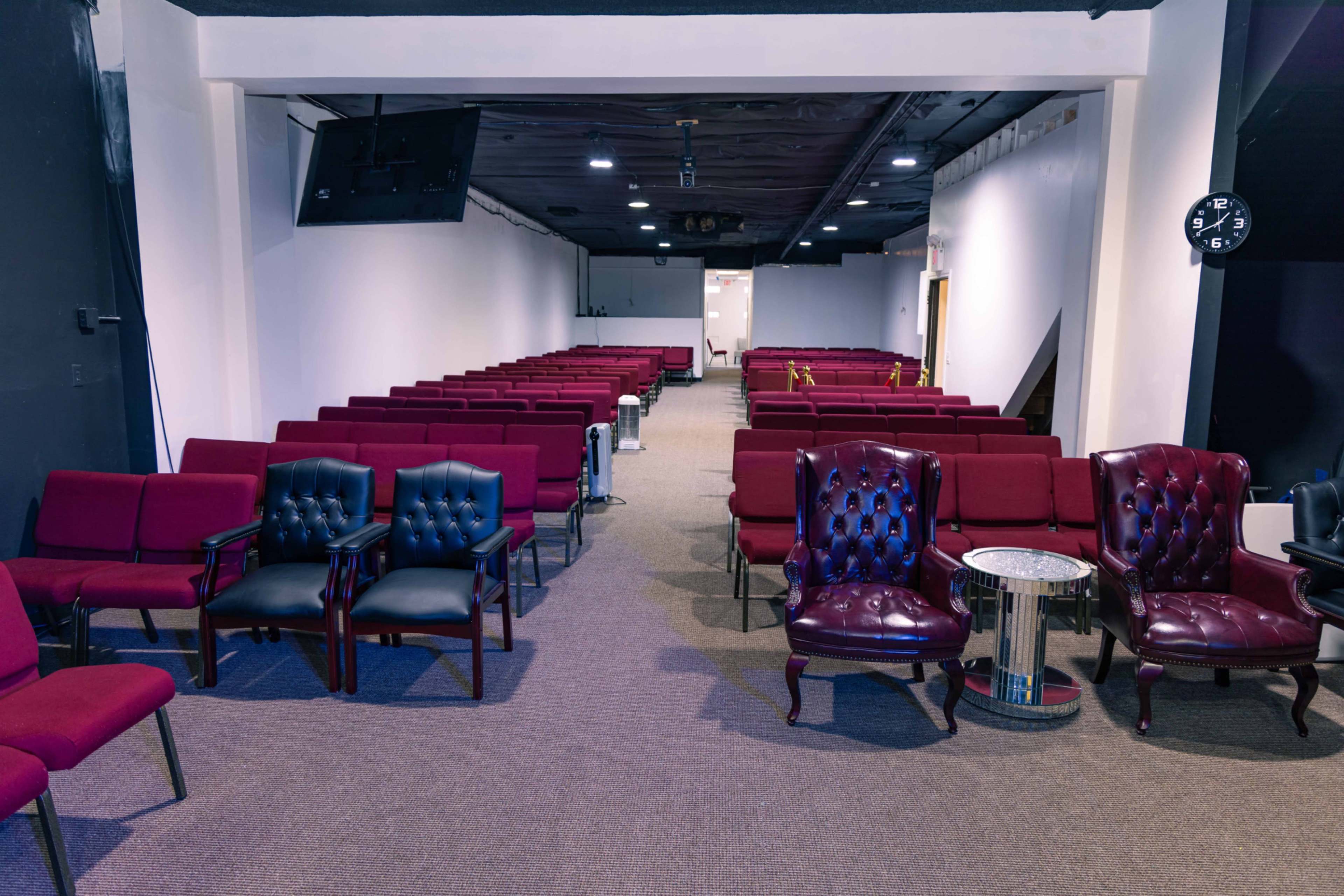 A spacious auditorium with rows of maroon chairs and a few ornate burgundy armchairs on either side.