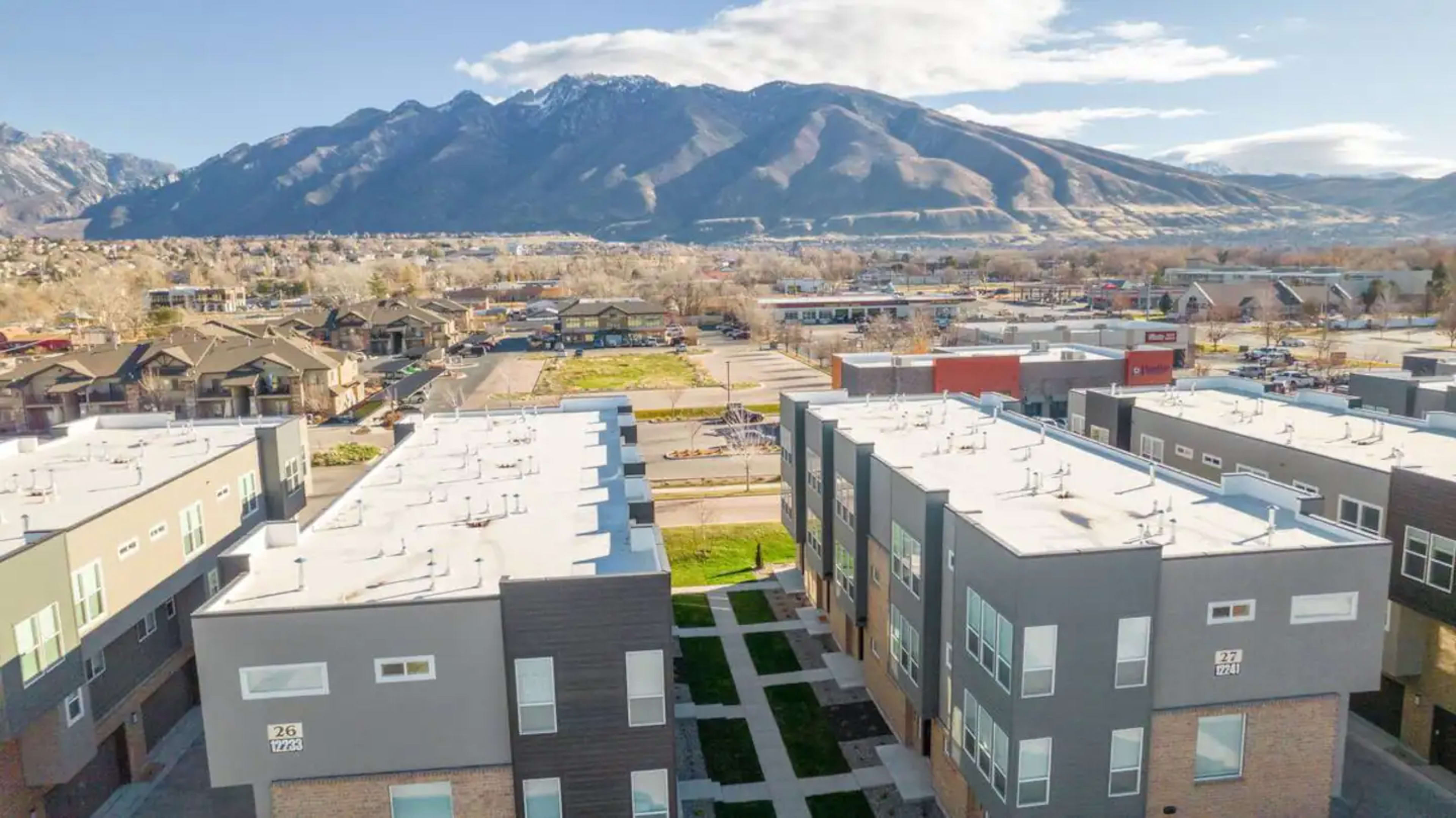 A row of modern apartment buildings is lined up in the foreground, with a mountainous landscape and valley view stretching behind them.