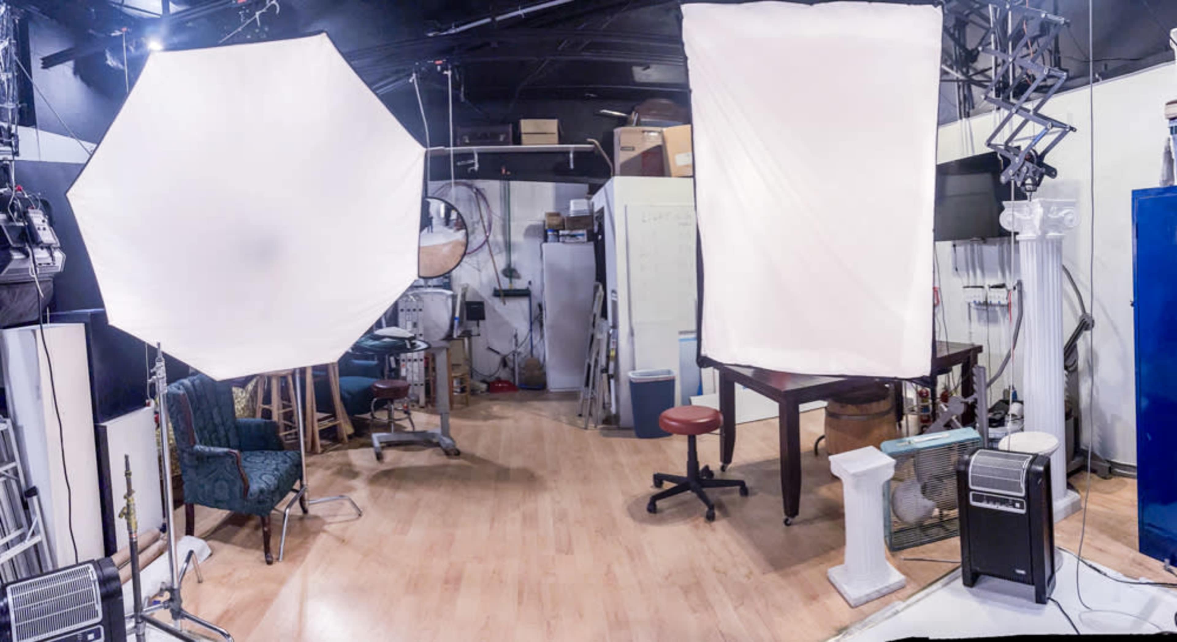 The image shows a studio space with two large softbox lights, a table, and various equipment, including a chair and a blue cabinet.