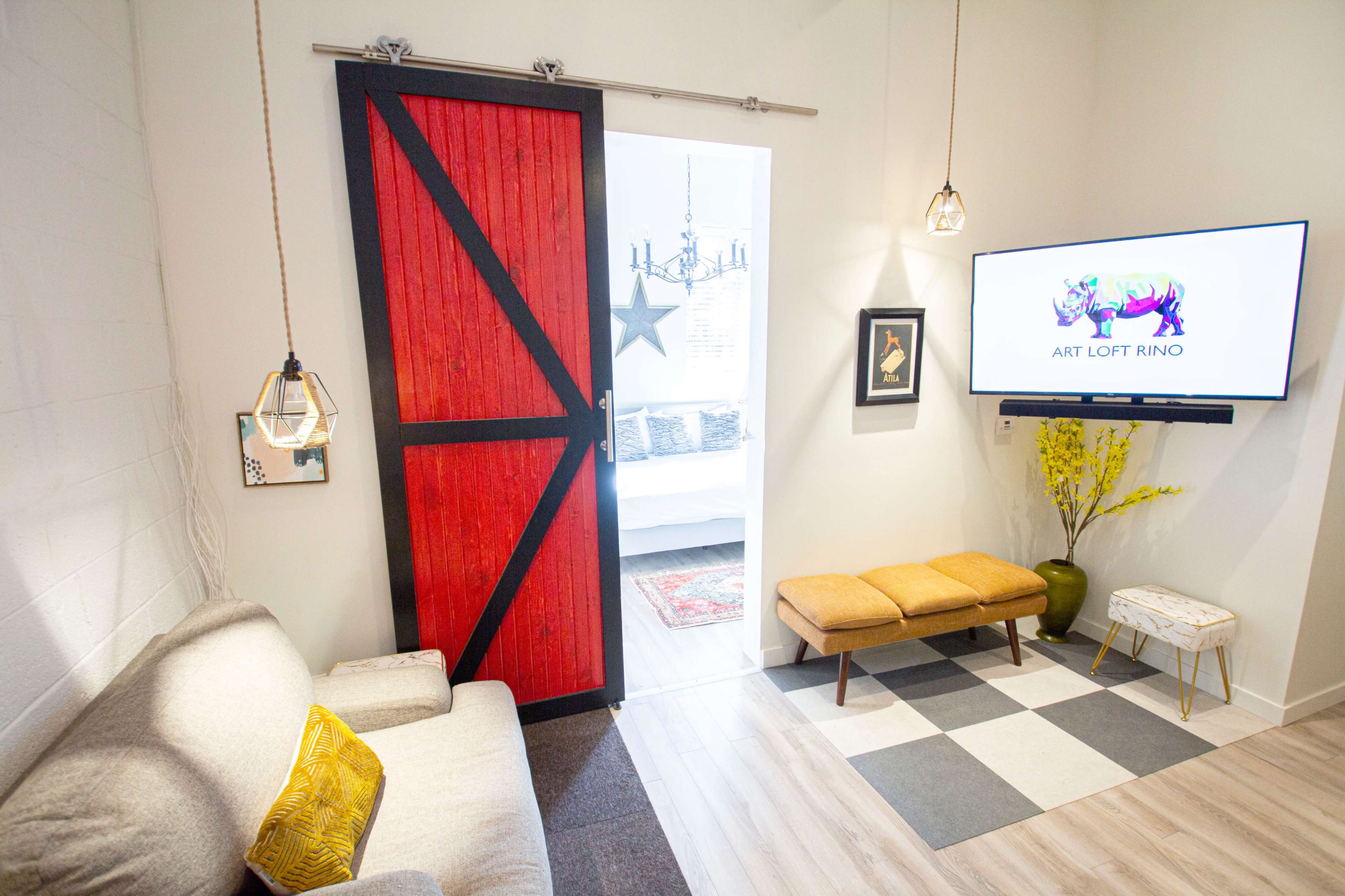 The image shows a modern room featuring a red sliding barn door, a television mounted on the wall, a beige couch, and a patterned floor.