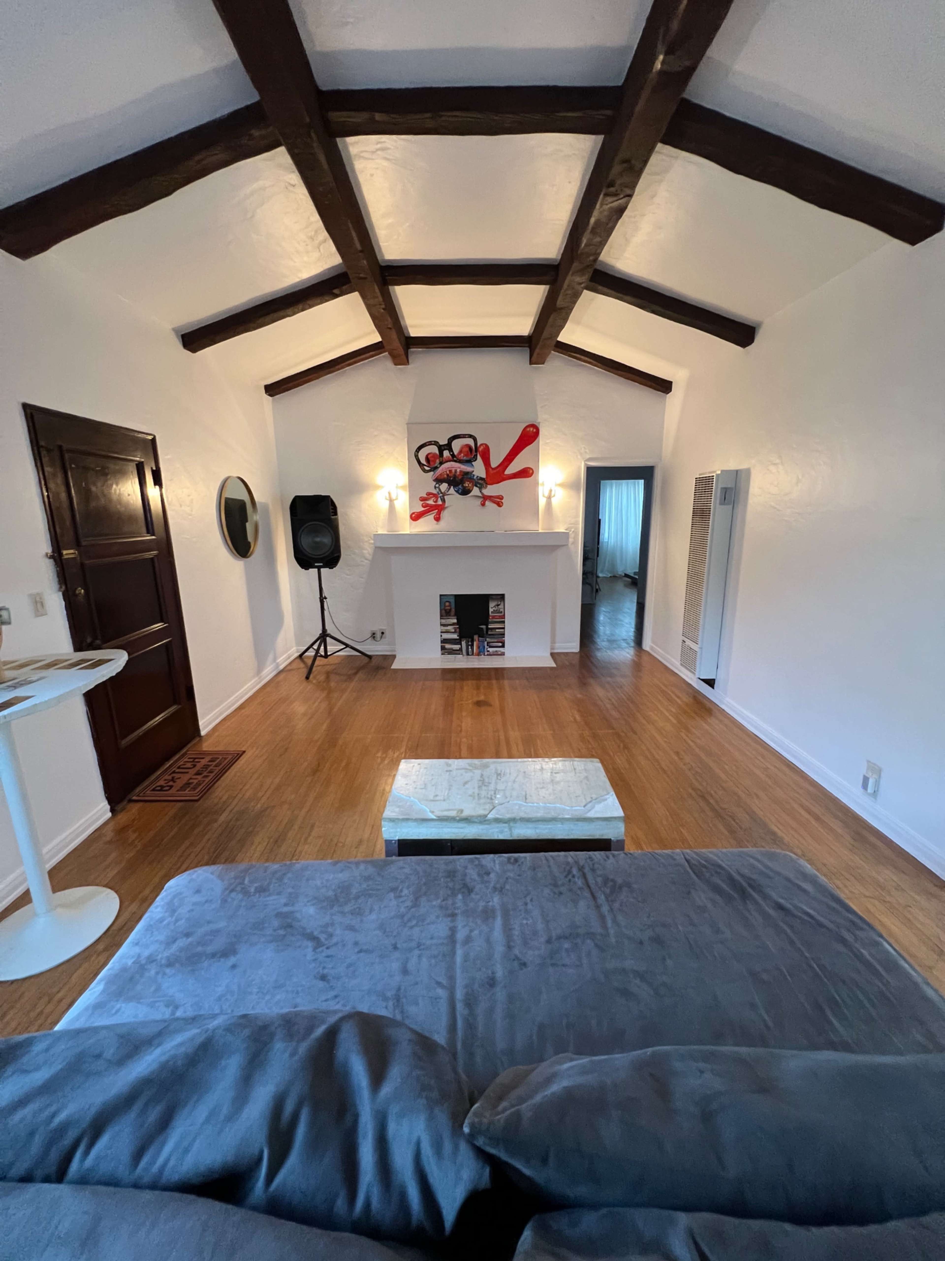 A spacious living room with wooden beam ceilings, a white fireplace, and a gray sofa facing a coffee table.