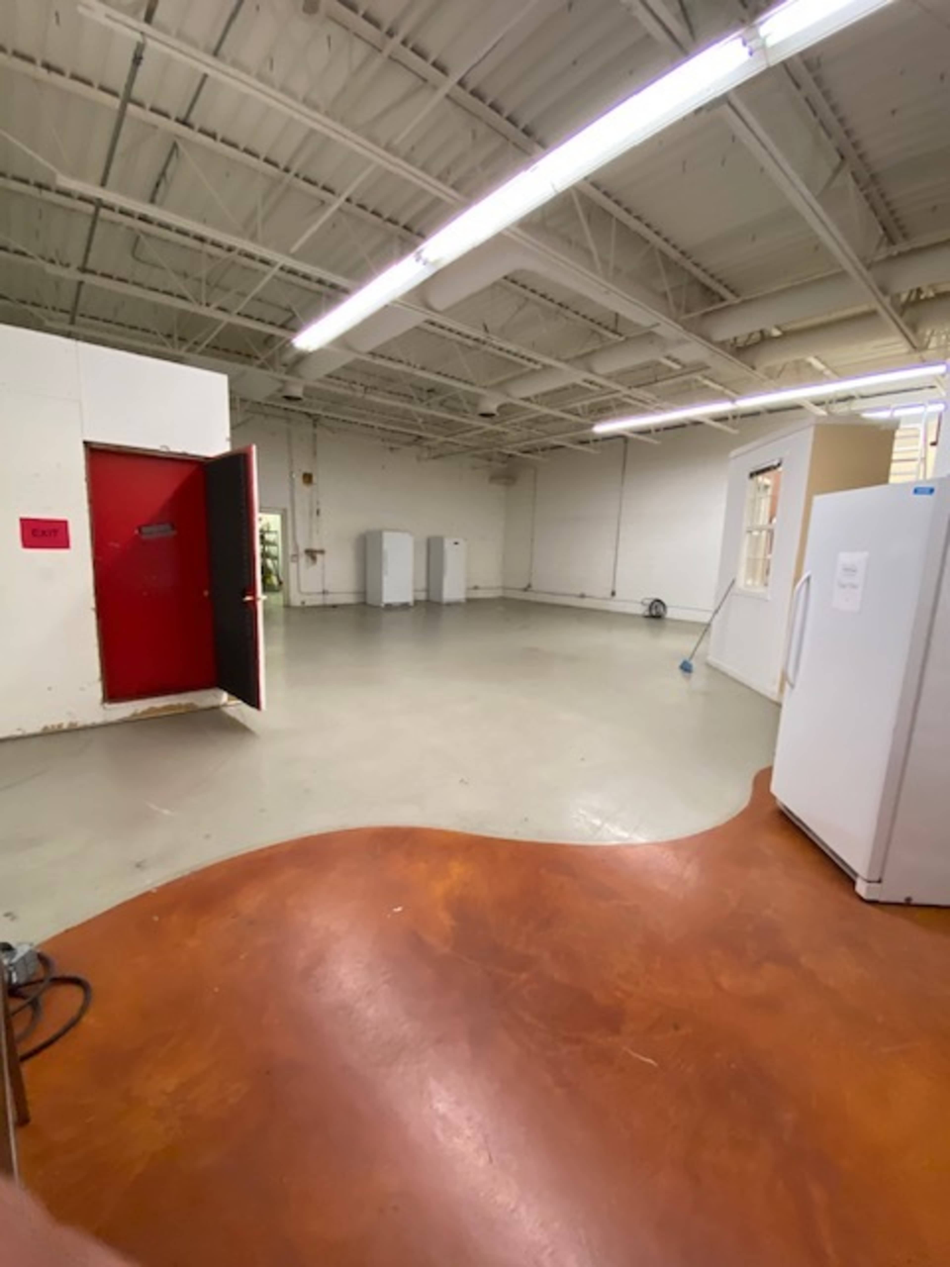 An empty room with a red door, two refrigerators, and a polished concrete floor.