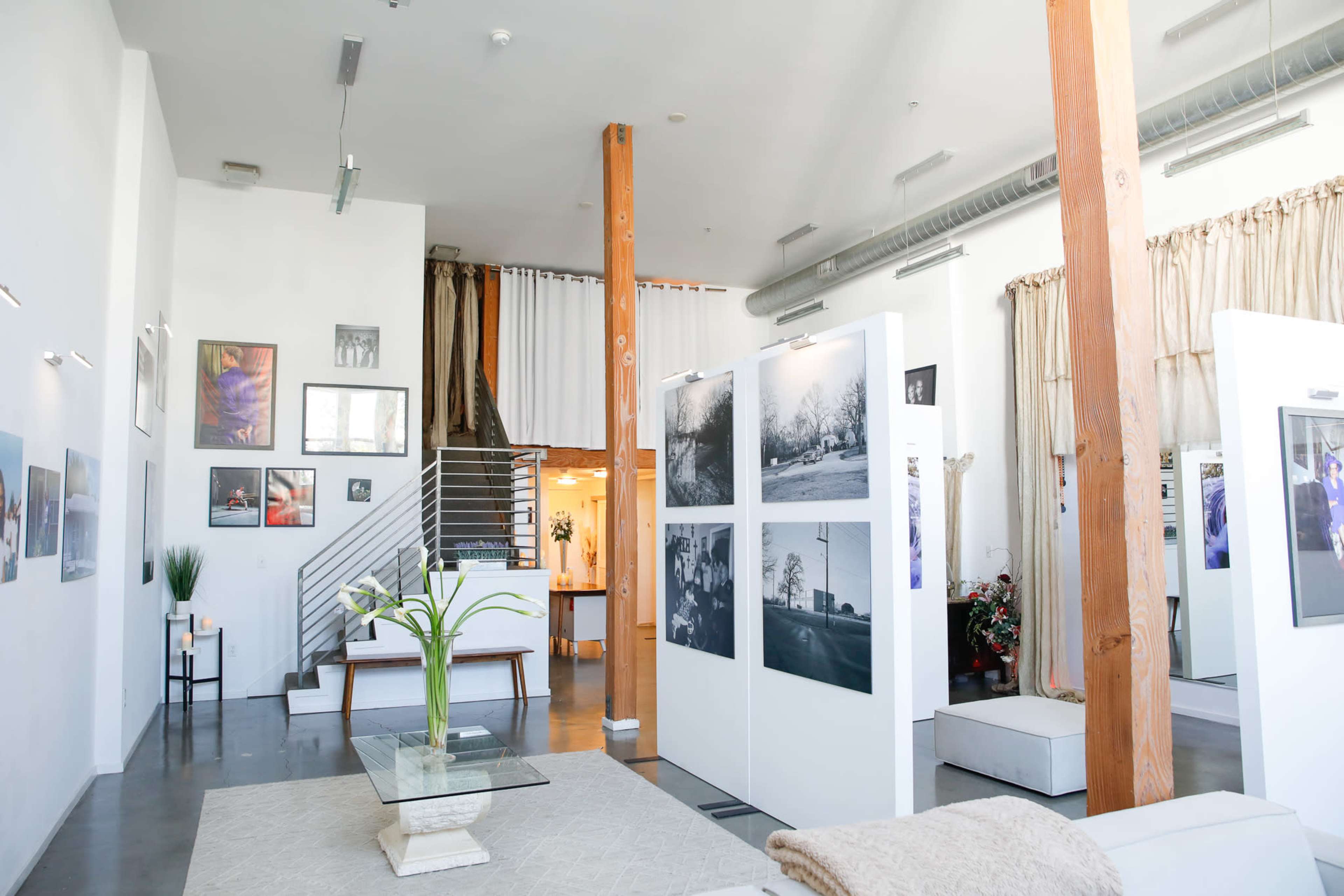 A modern art gallery with white walls, large photographs displayed on partition panels, and wooden beams in the ceiling.