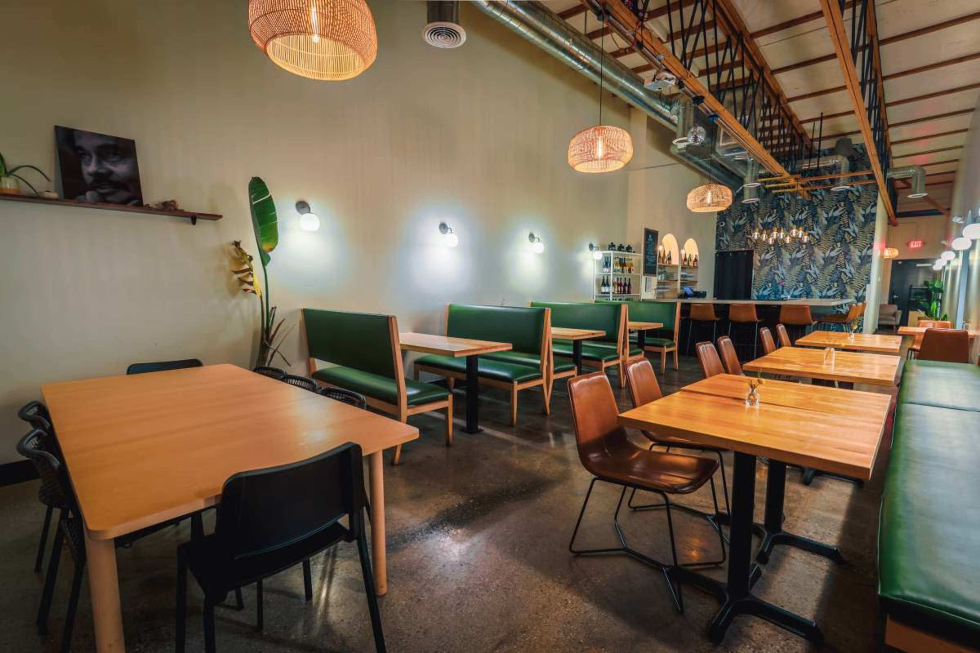 The image shows a modern restaurant interior with wooden tables, green benches, and decorative lighting.