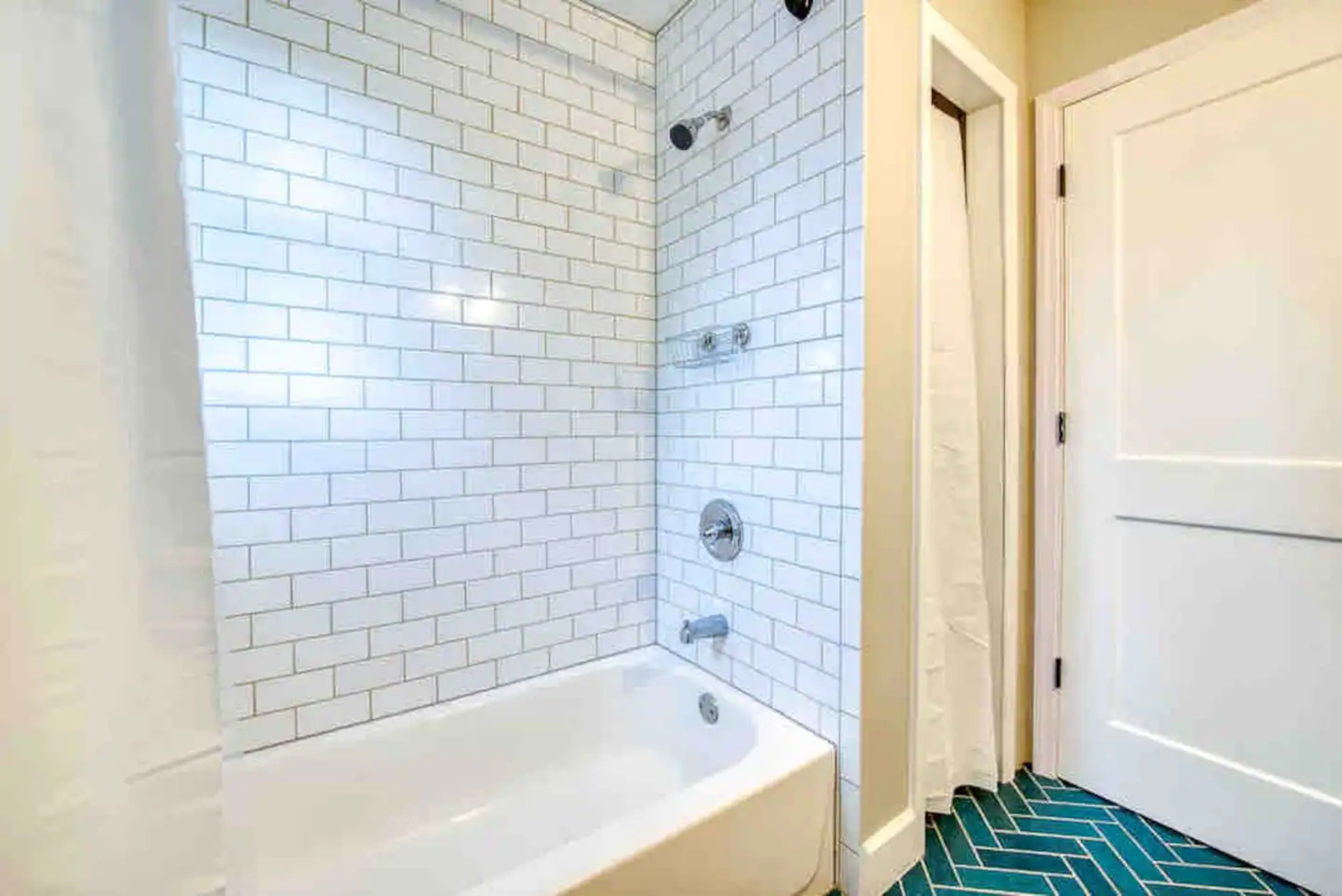 A bathroom with a white tiled shower area, a bathtub, and a blue patterned floor.