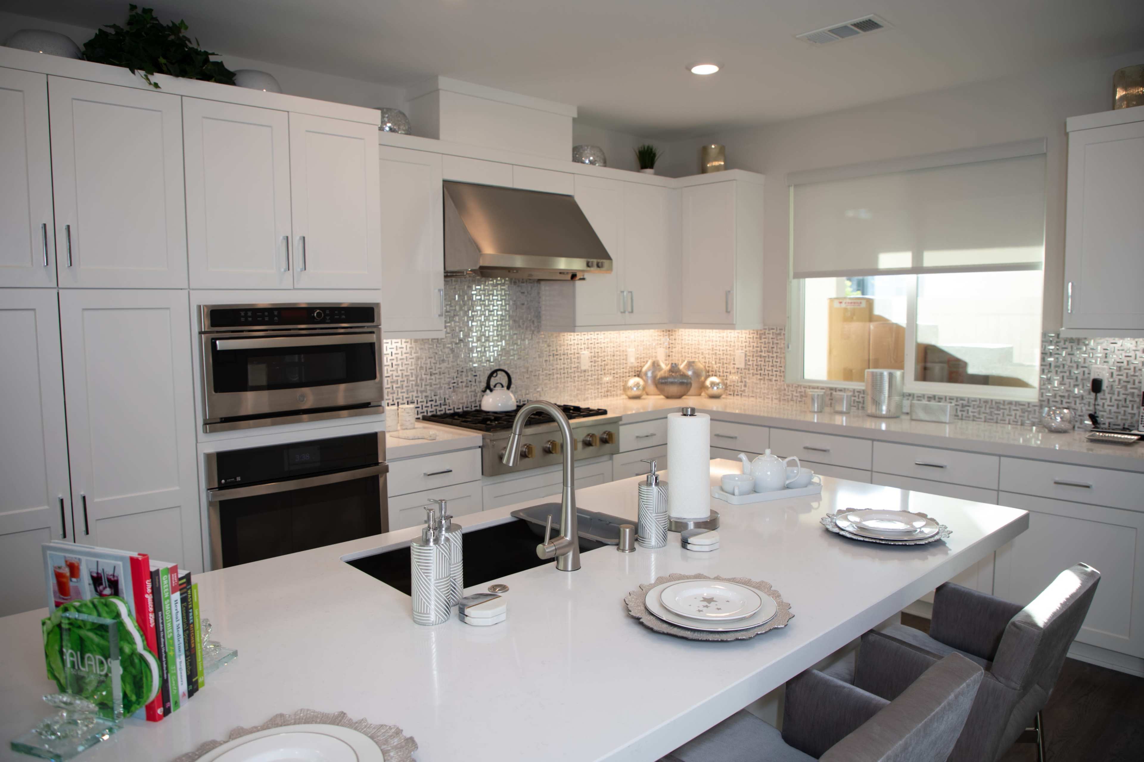 A modern kitchen with white cabinetry, stainless steel appliances, a large island with seating, and a tiled backsplash.