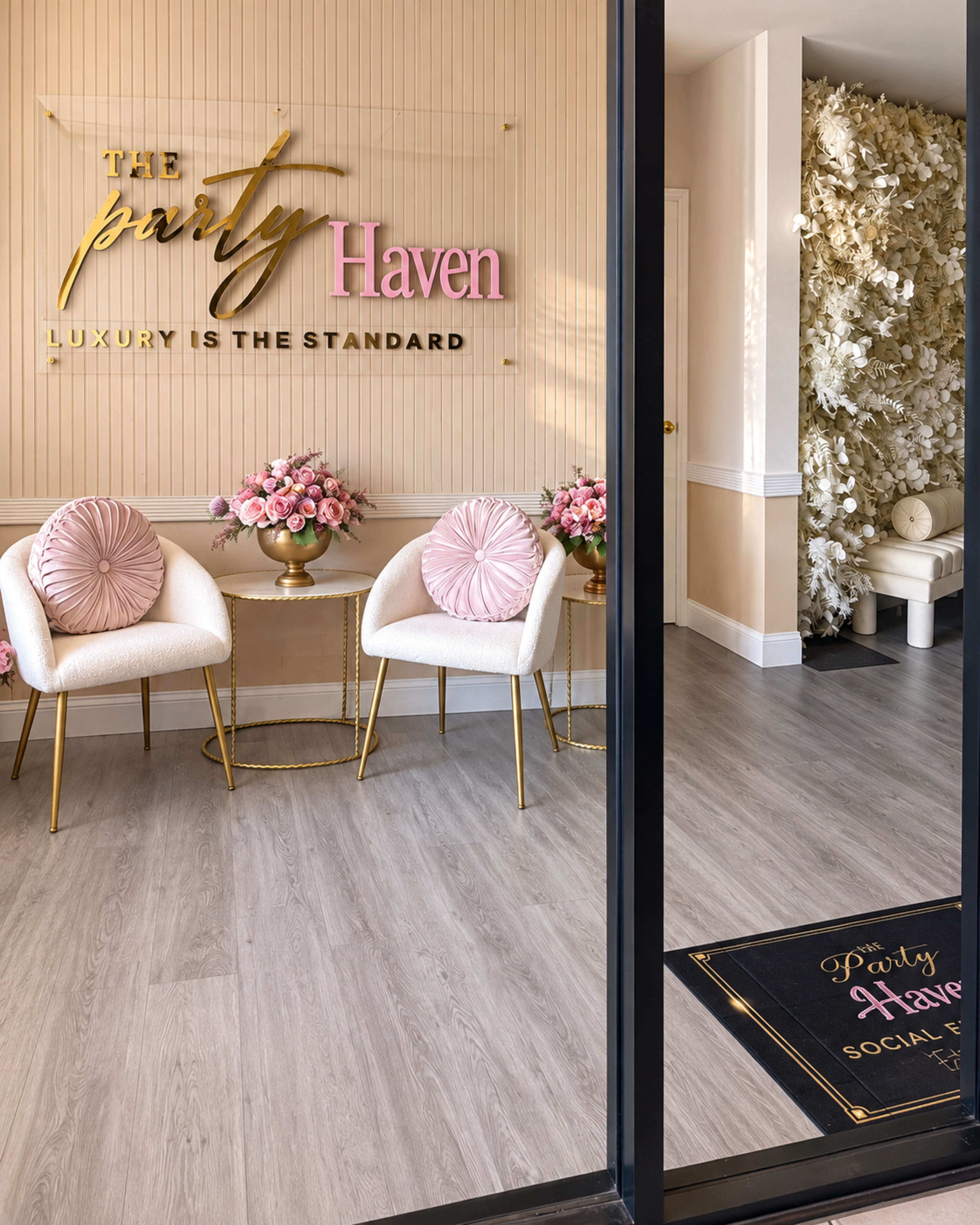 The image shows a stylish interior of a venue called "The Party Haven," featuring two white chairs with pink cushions and floral arrangements, along with a decorative wall adorned with white flowers.