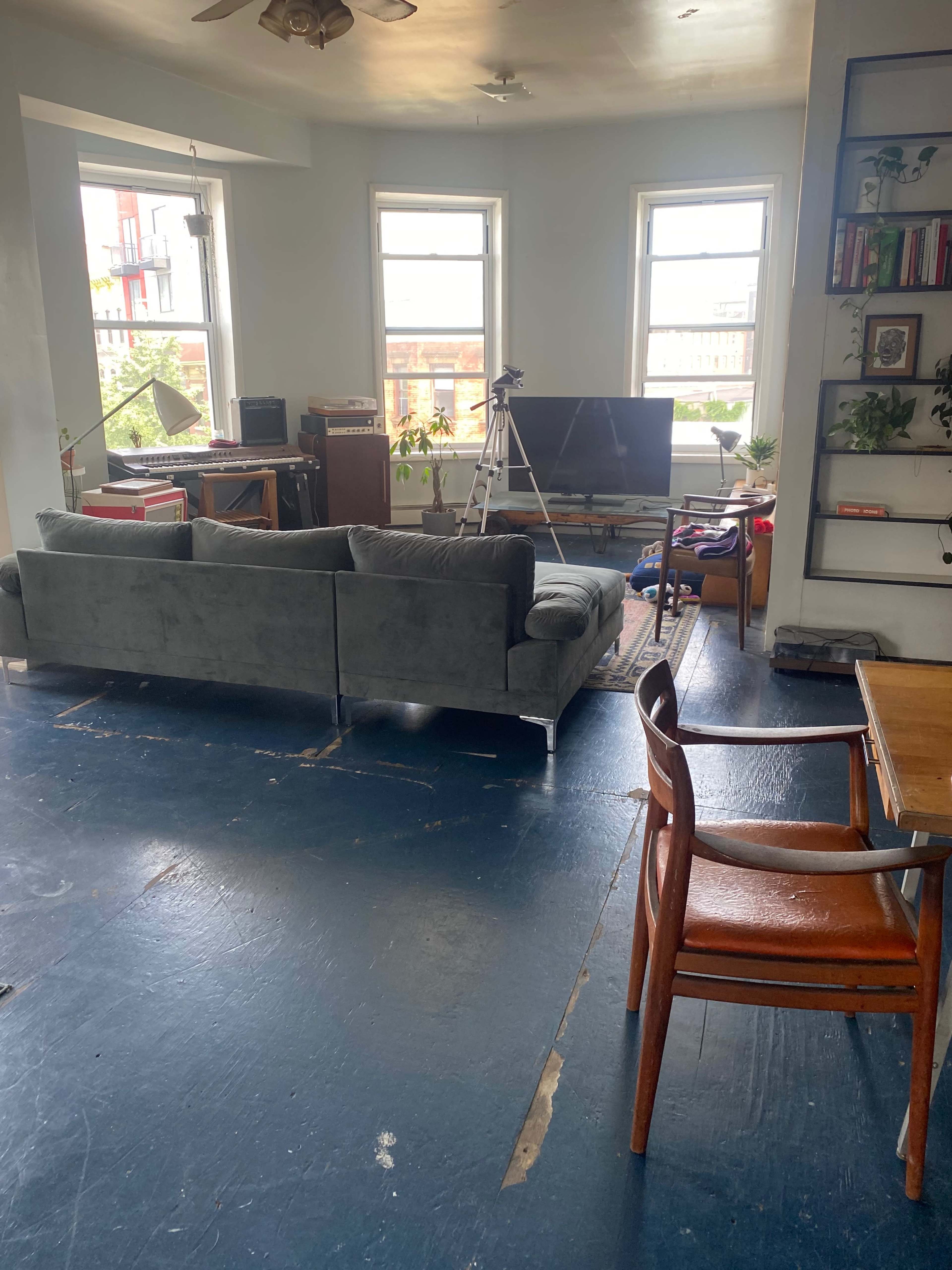 A living room with a gray sofa facing a television on a stand, while a wooden table and chair are positioned nearby.