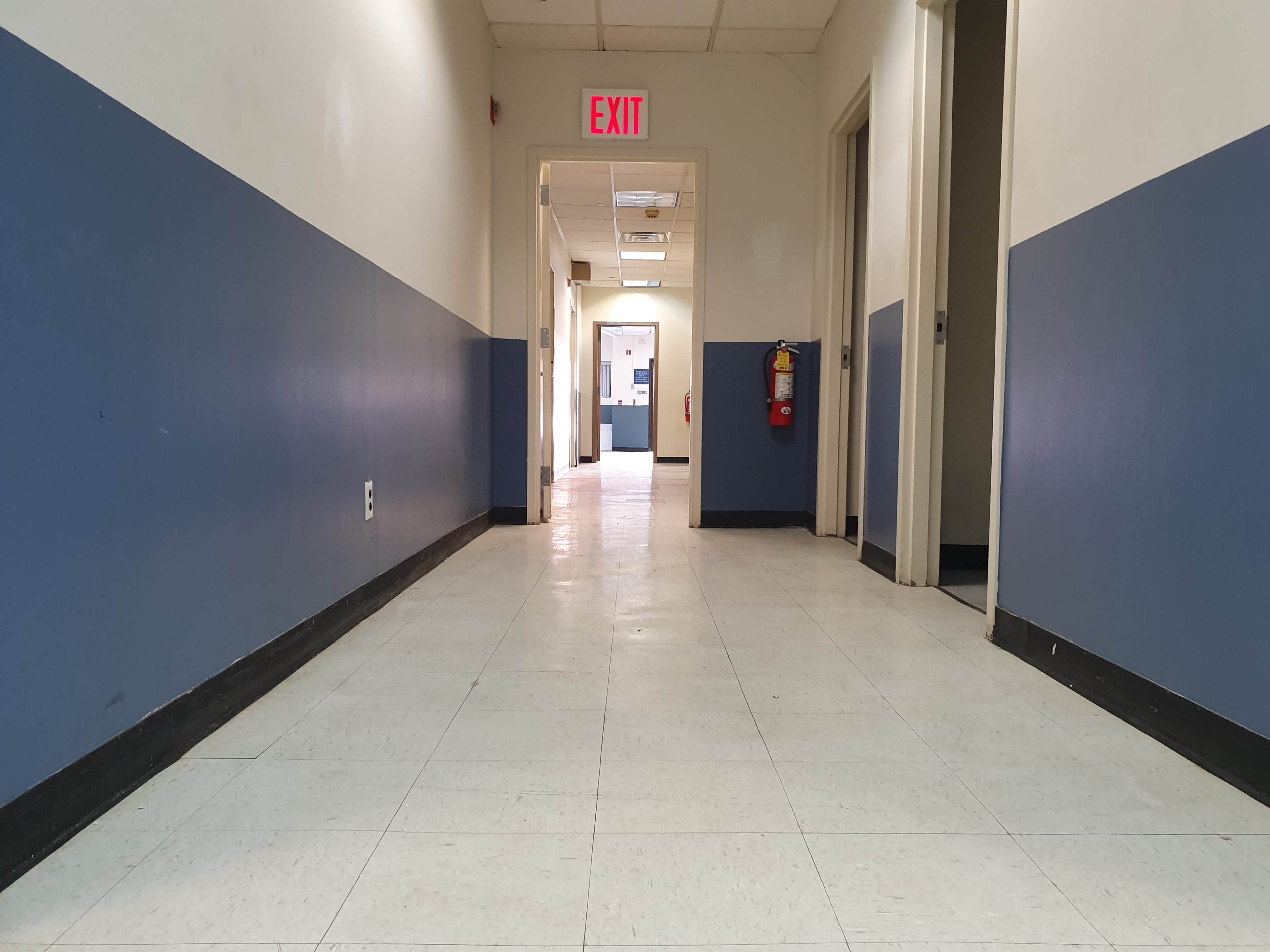 A long corridor with blue and white walls leads to an exit door at the far end.