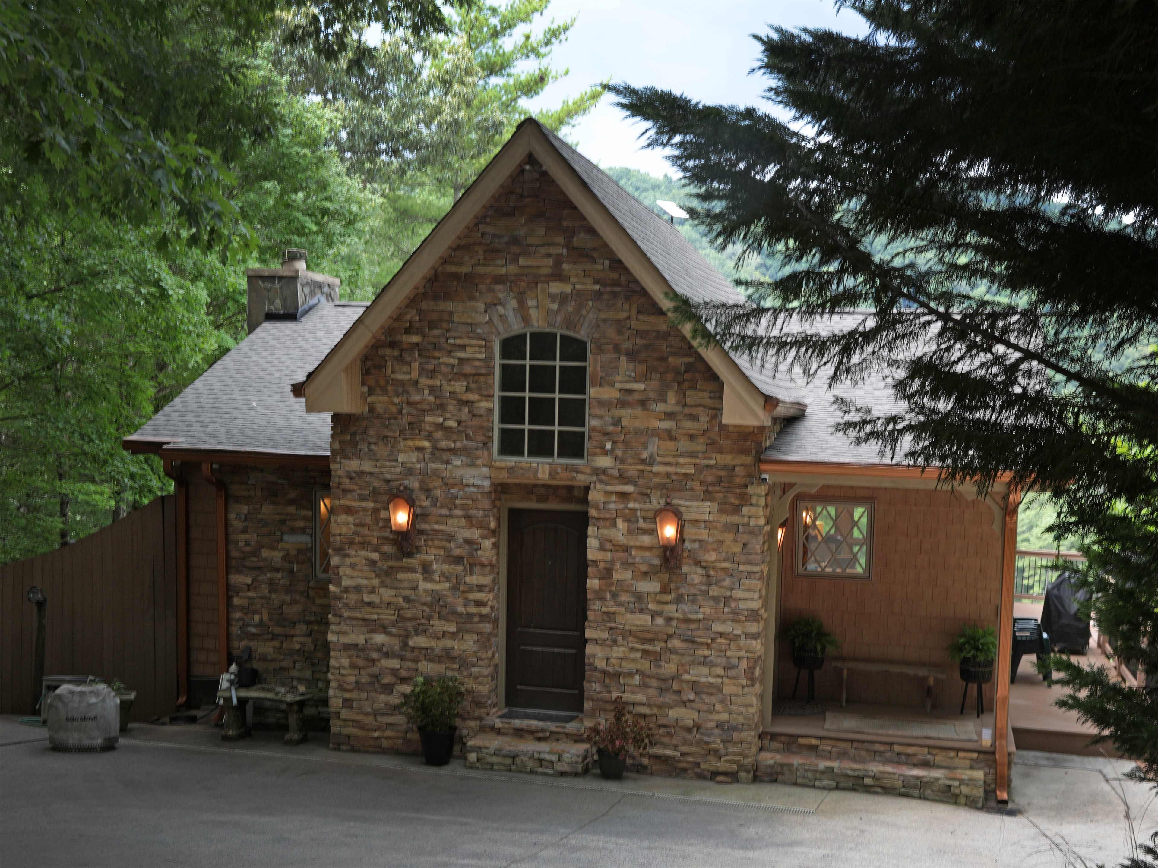 A stone-faced house with a wooden door, surrounded by trees.