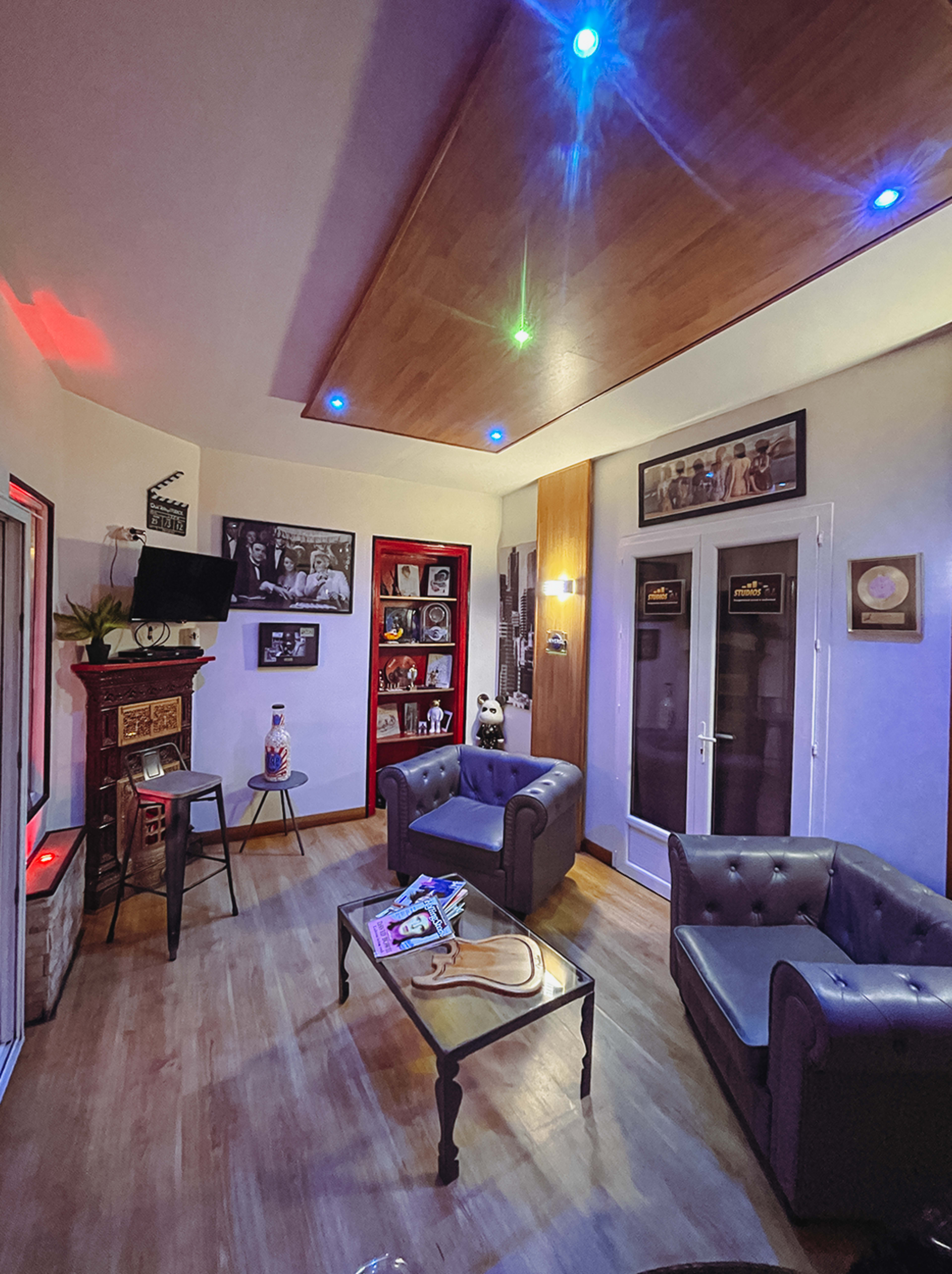 The image shows a modern living room with two leather sofas, a coffee table, and shelves displaying various decorations, all illuminated by colorful ceiling lights.