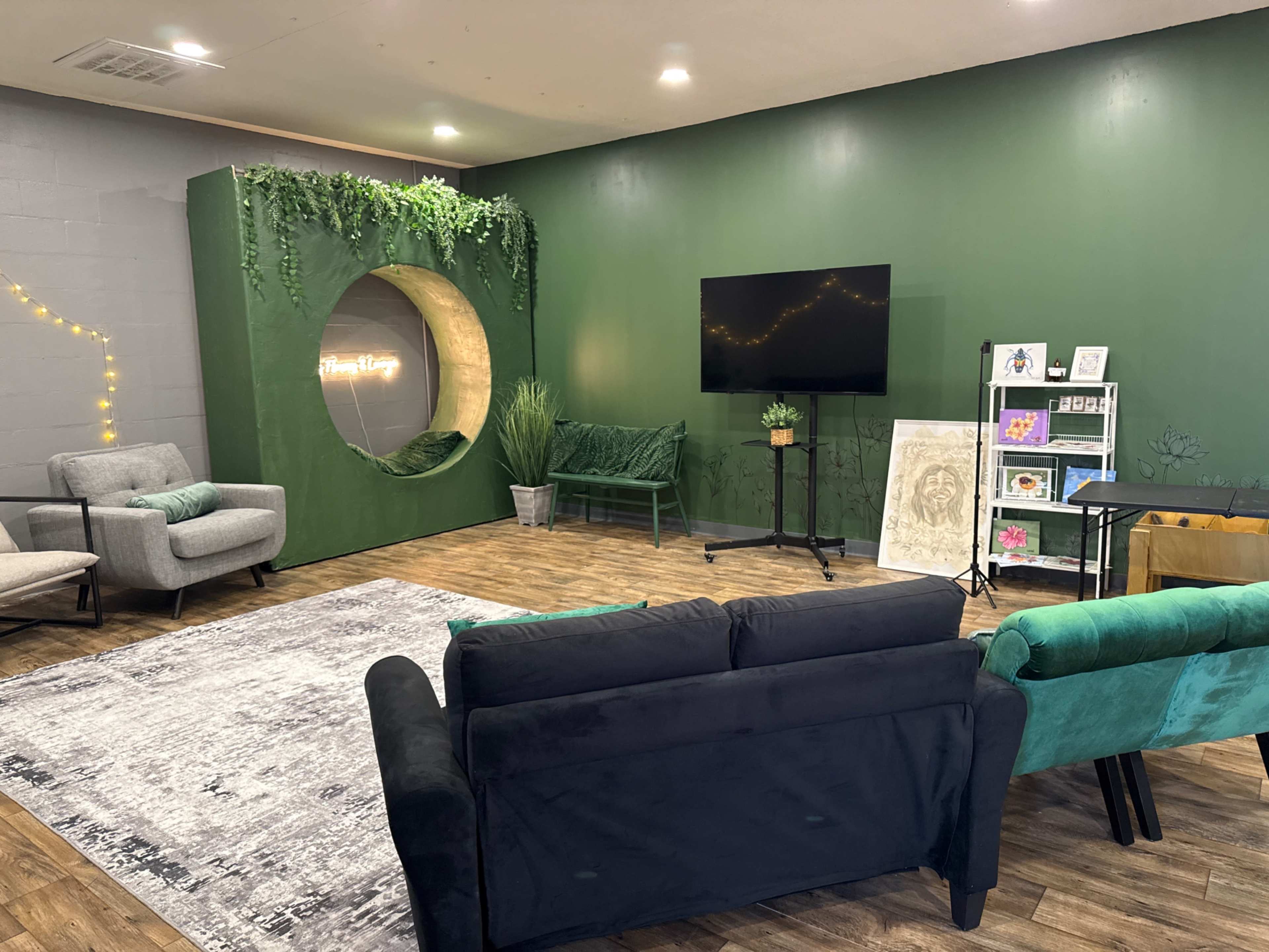 The image shows a cozy indoor space featuring green walls, modern furniture, a television on a stand, and decorative plants.