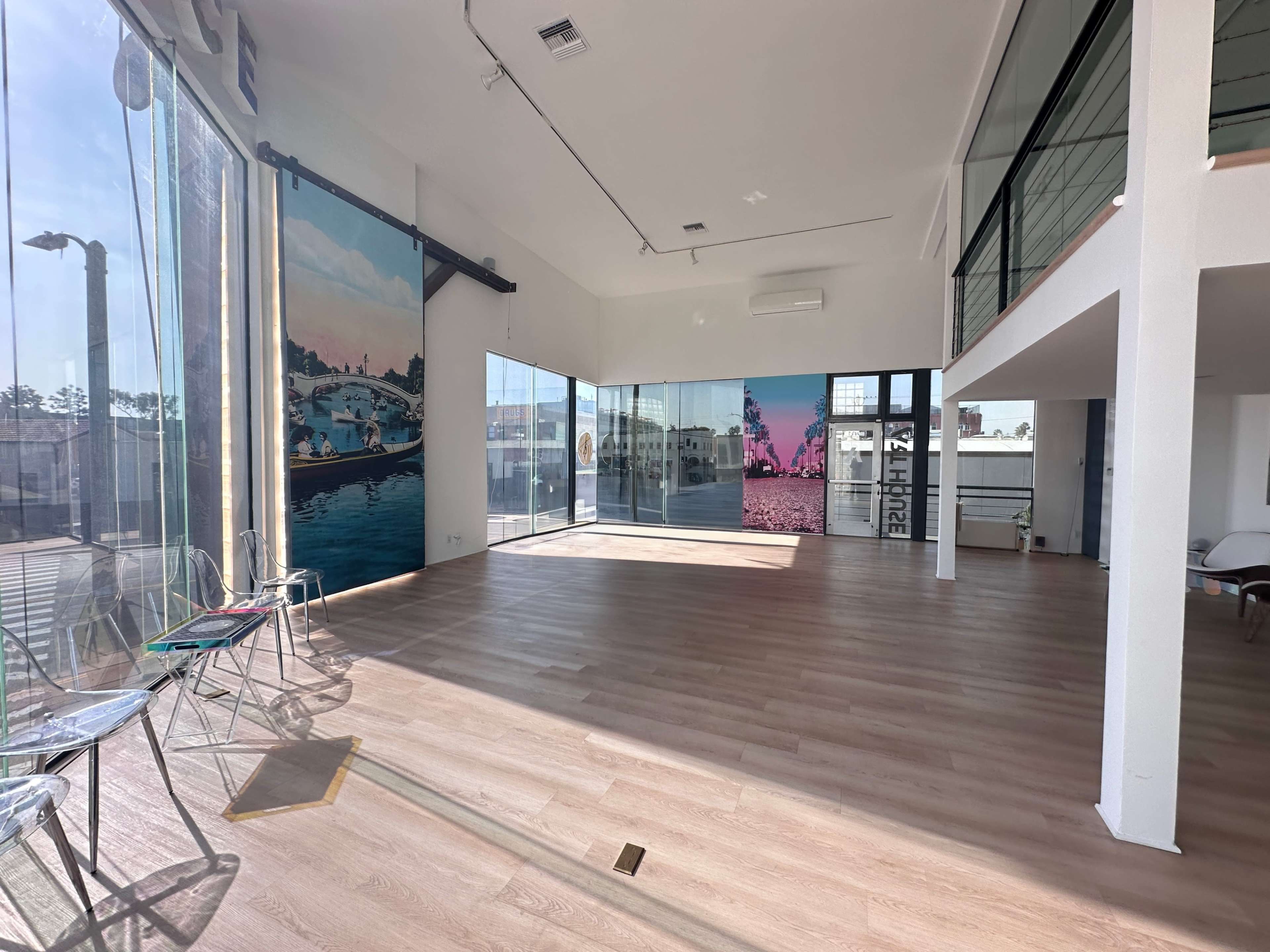 The image shows a spacious, brightly lit interior with large windows and modern decor, featuring murals on the walls and wooden flooring.