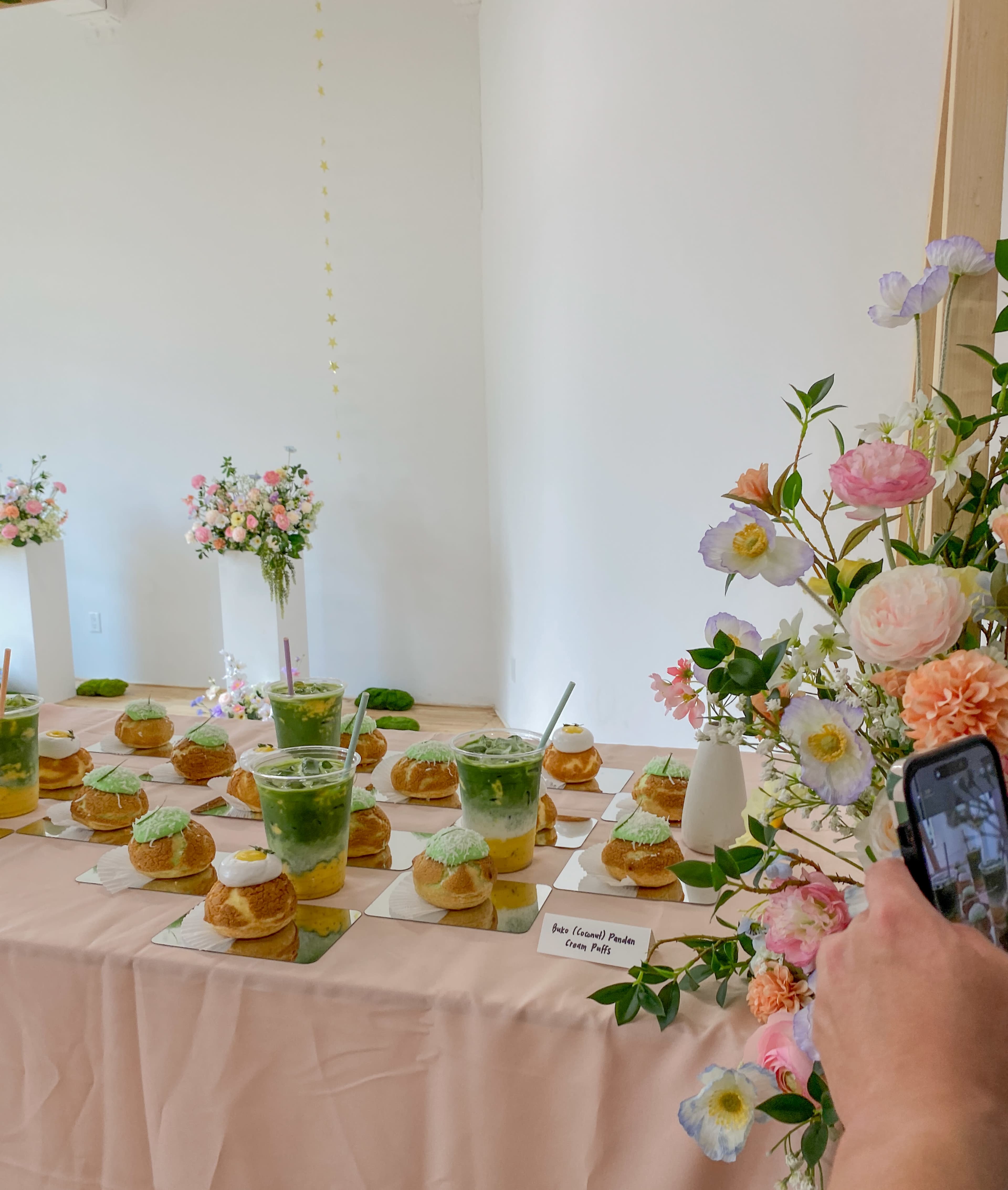 A table is adorned with green beverages and pastries, surrounded by flower arrangements in vases.