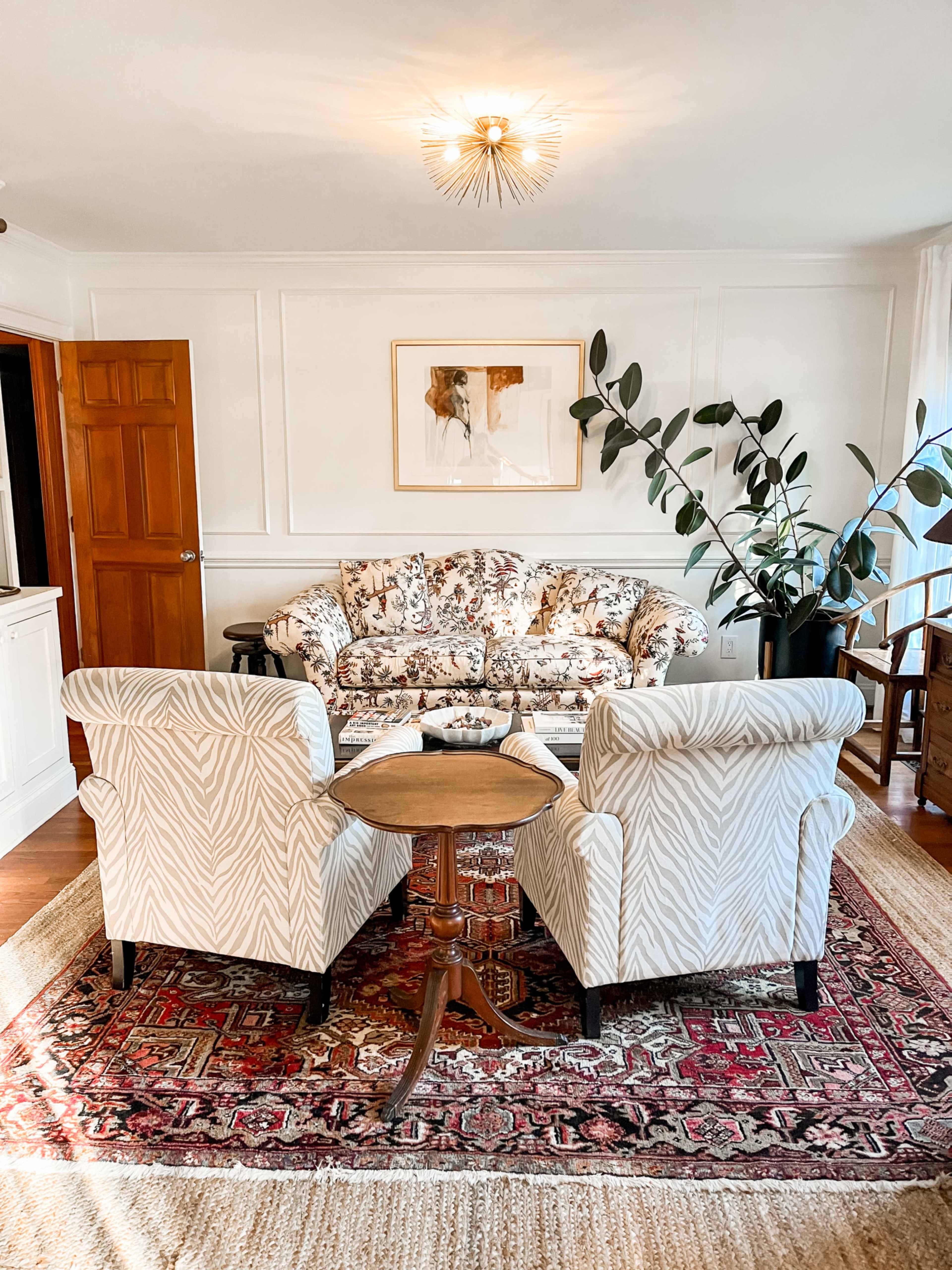 A floral-patterned sofa with two striped armchairs and a circular table is arranged on a patterned rug in a well-lit living room.