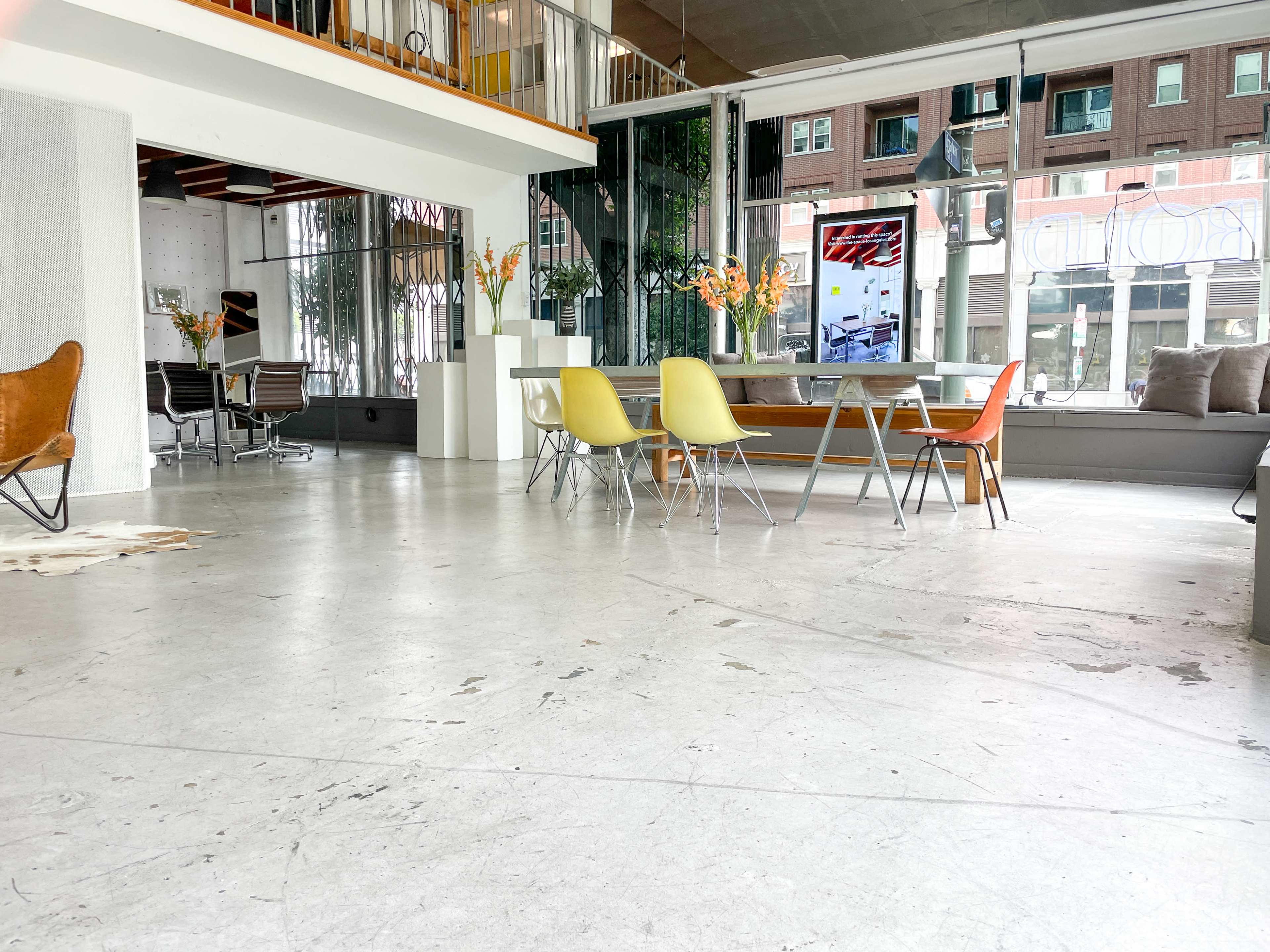 The image shows a spacious interior featuring a dining area with a large table and colorful chairs, surrounded by large windows and modern décor.