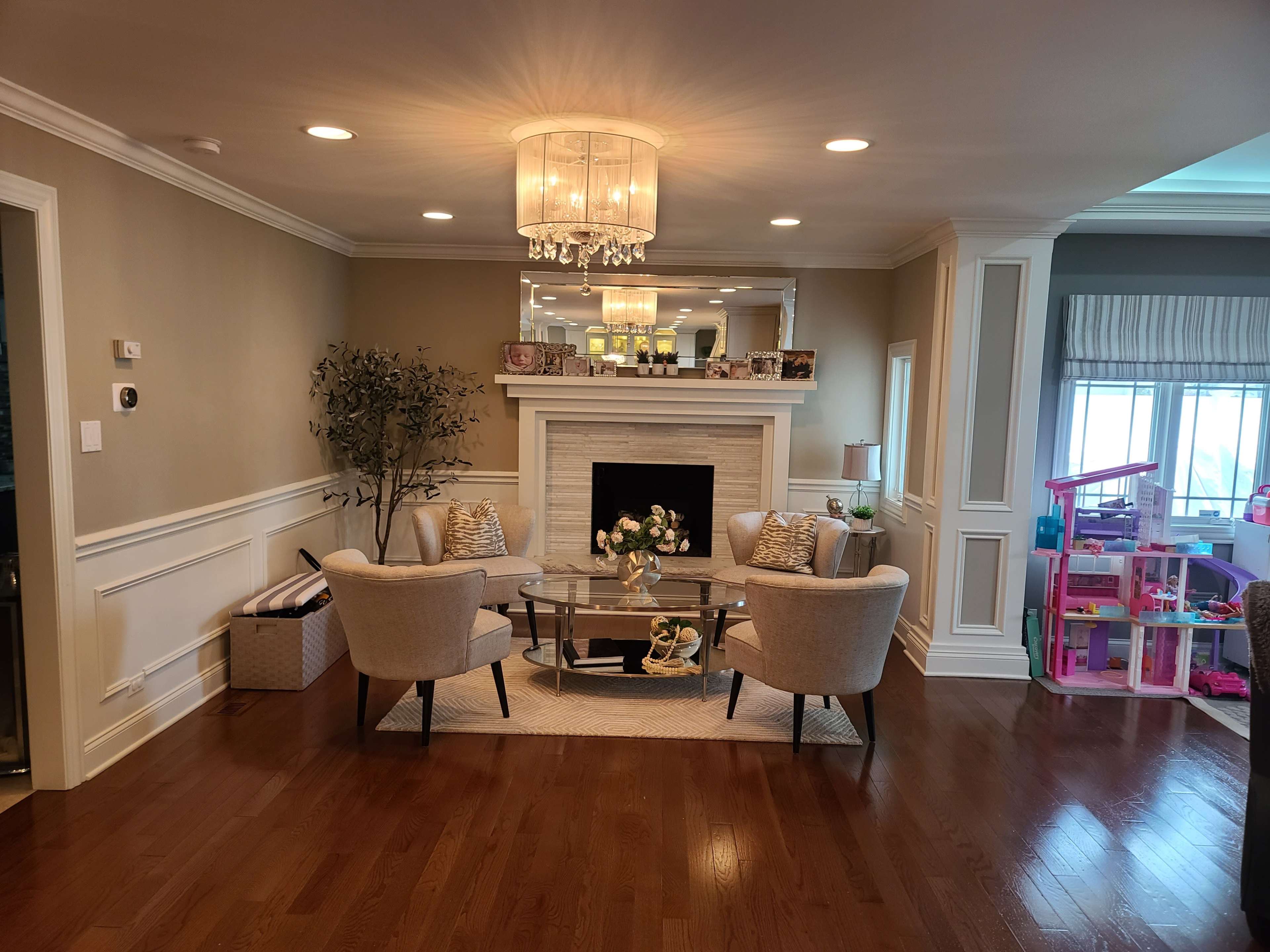 The image shows a living room featuring two armchairs and a coffee table arranged around a fireplace, with a play area visible in the background.