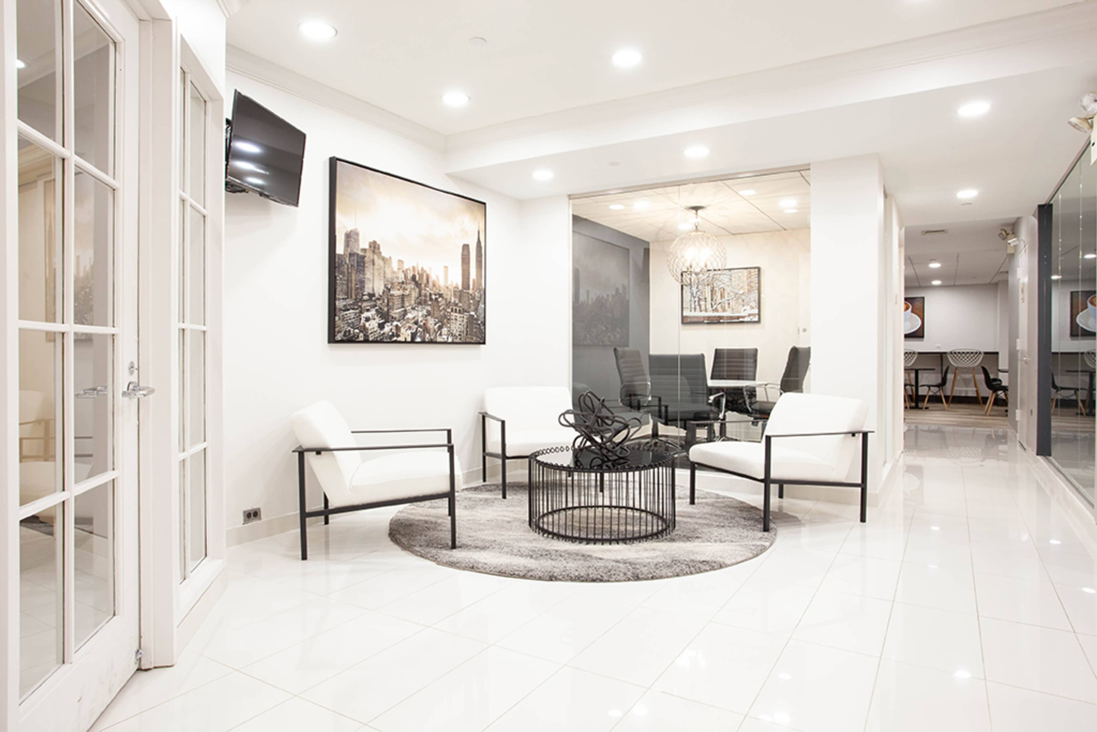 The image shows a modern reception area featuring white chairs, a round coffee table, and a large wall art of a city skyline.