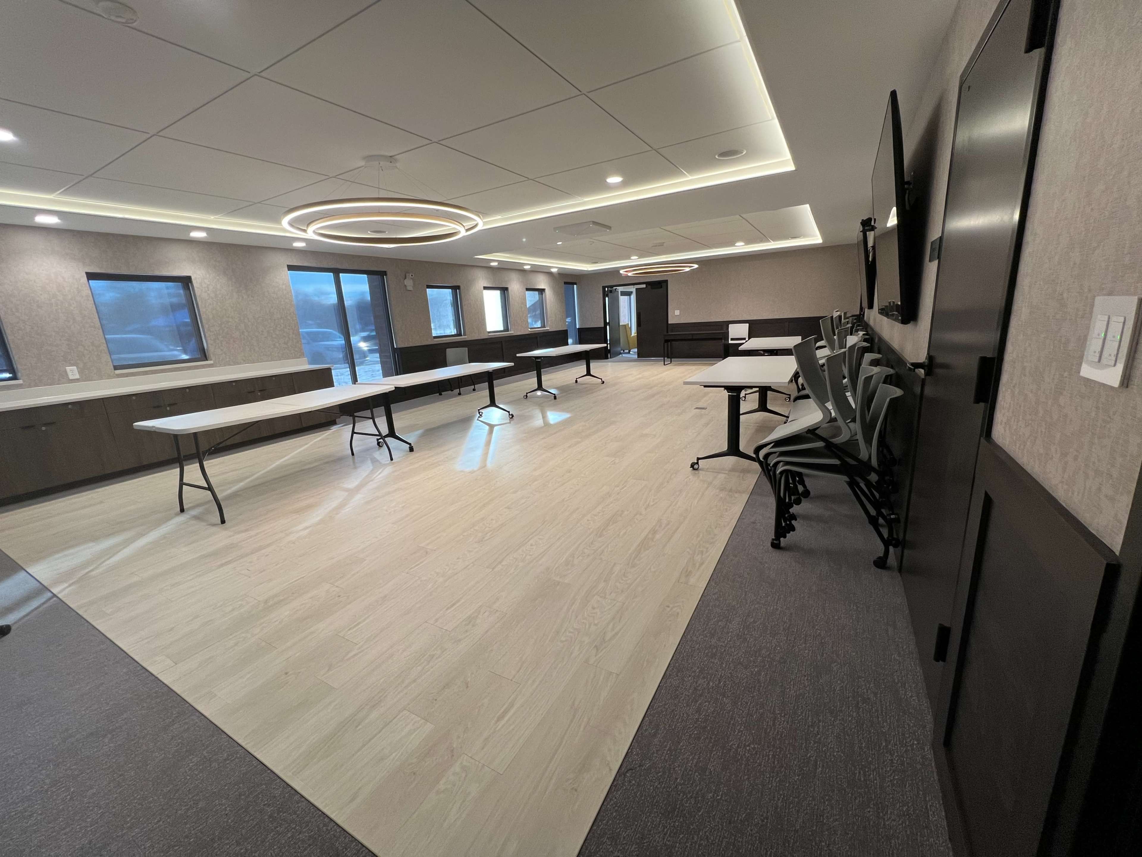 A conference room with several tables set up and stacked chairs against the wall, well-lit by overhead lights.