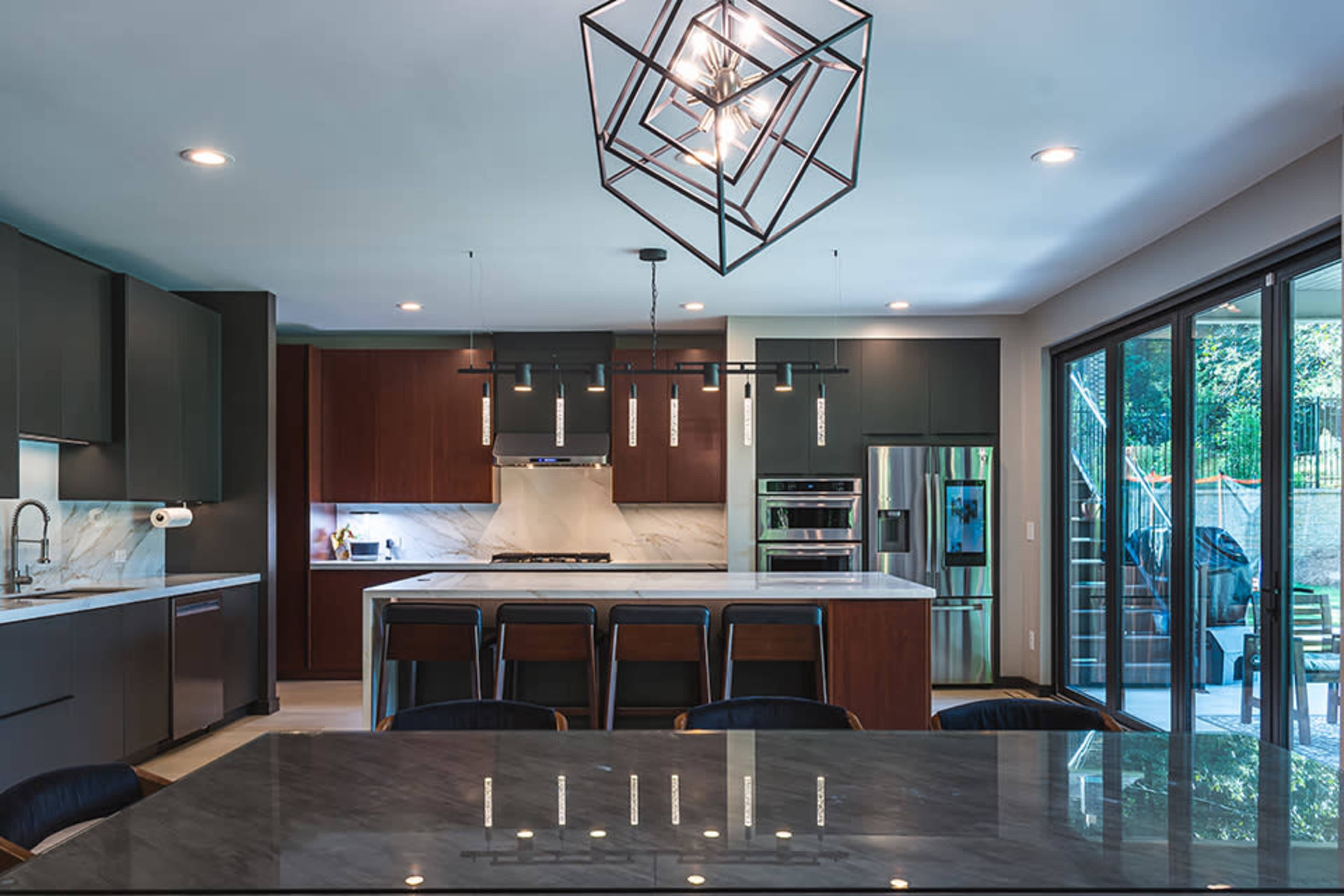 The modern kitchen features dark cabinetry, a large island with seating, and a multilight pendant fixture above the countertop.