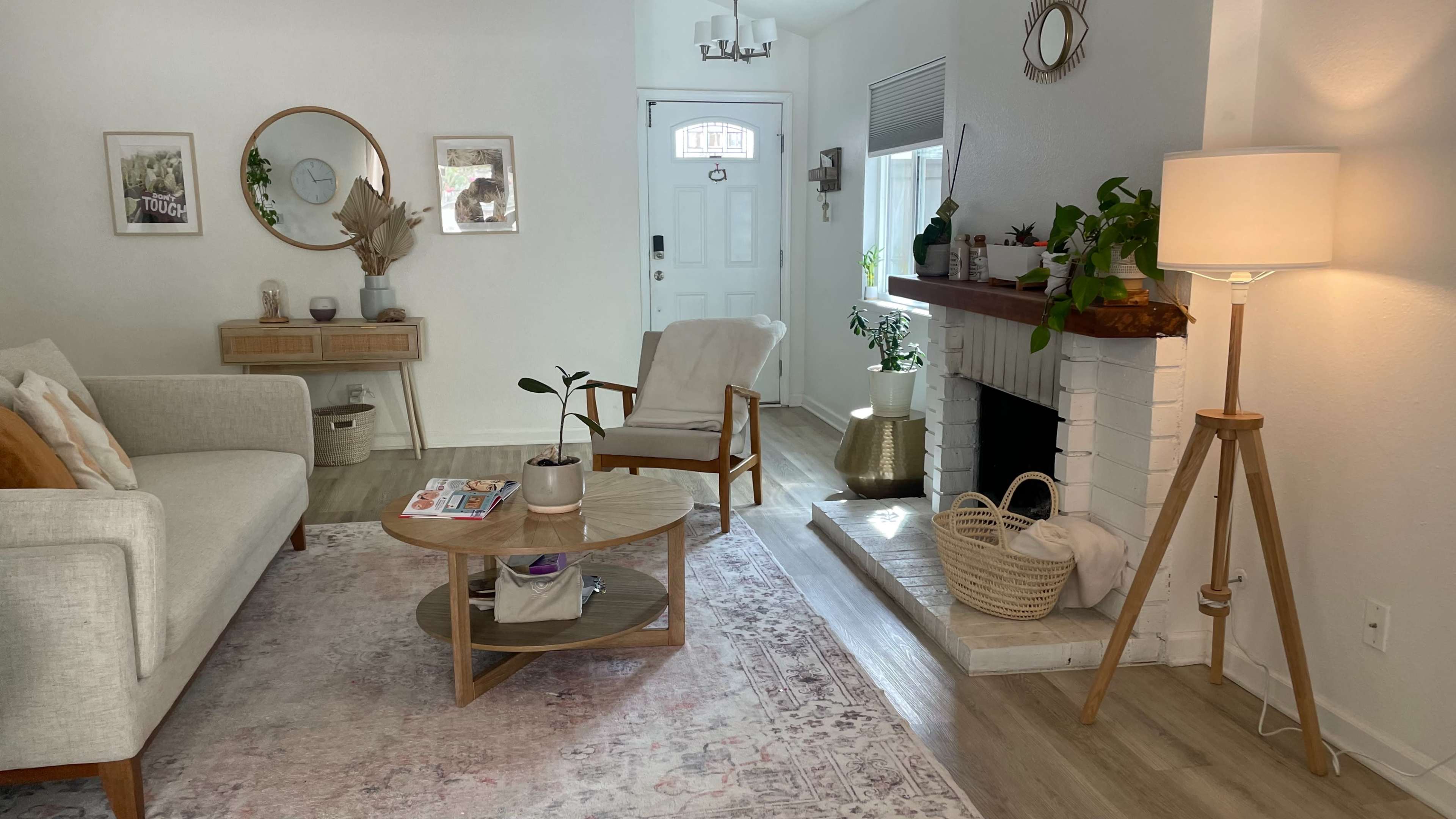 A modern living room with a neutral color palette, featuring a sofa, coffee table, fireplace, and decorative plants.