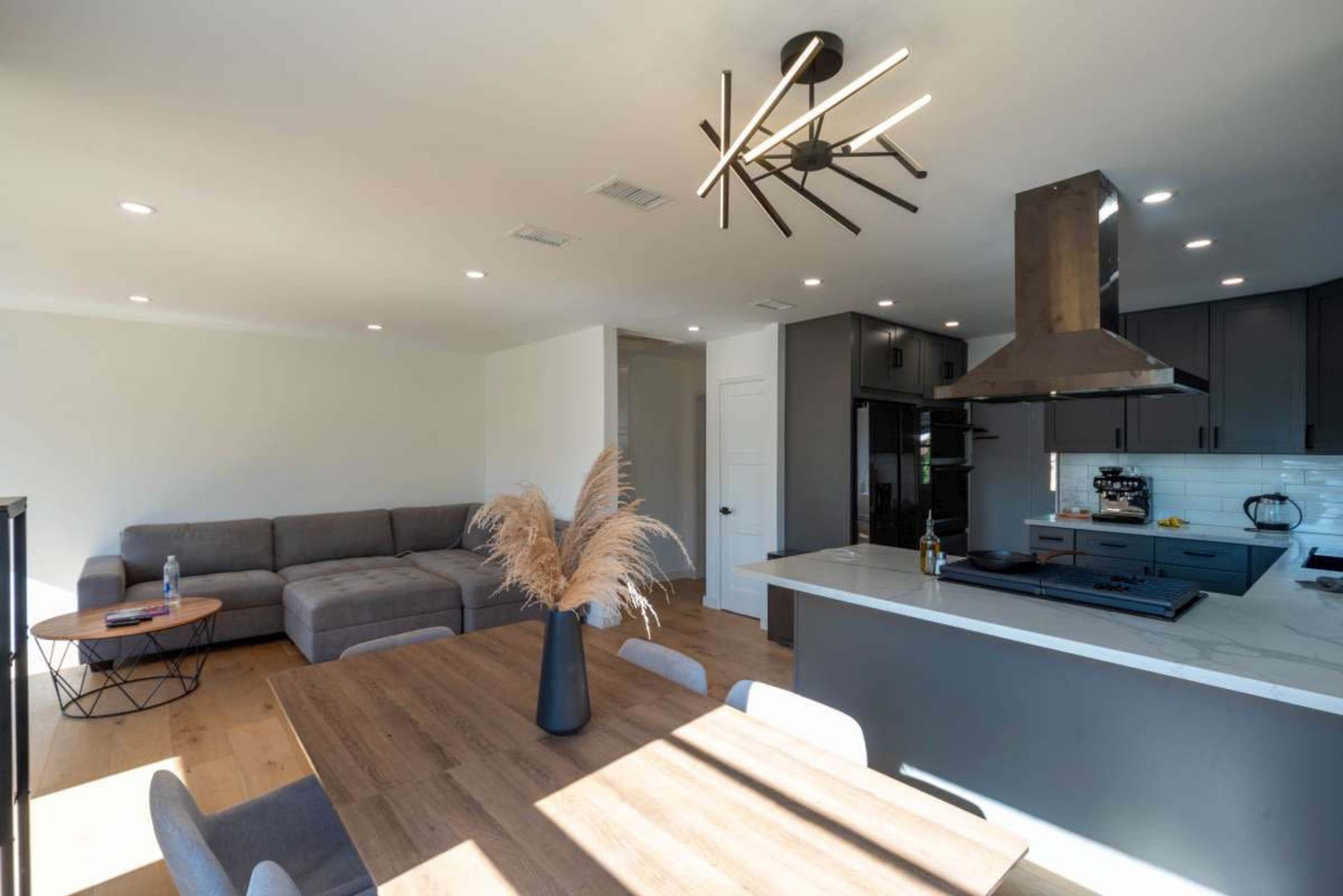 A modern open-concept living area featuring a sectional sofa, a dining table, and a kitchen with a central island and a range hood.