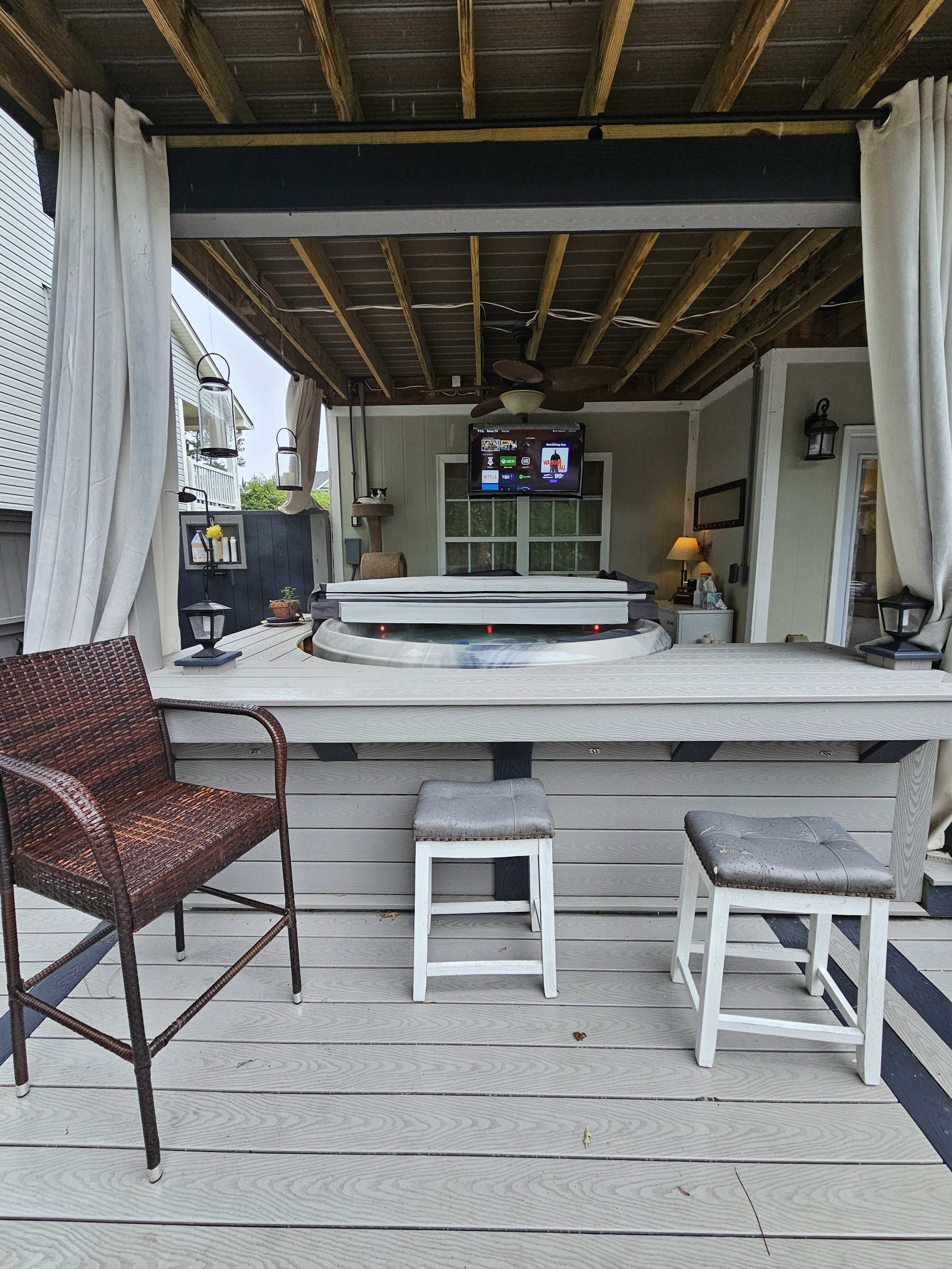 A covered patio area featuring a hot tub, two stools, and a television mounted on the wall.