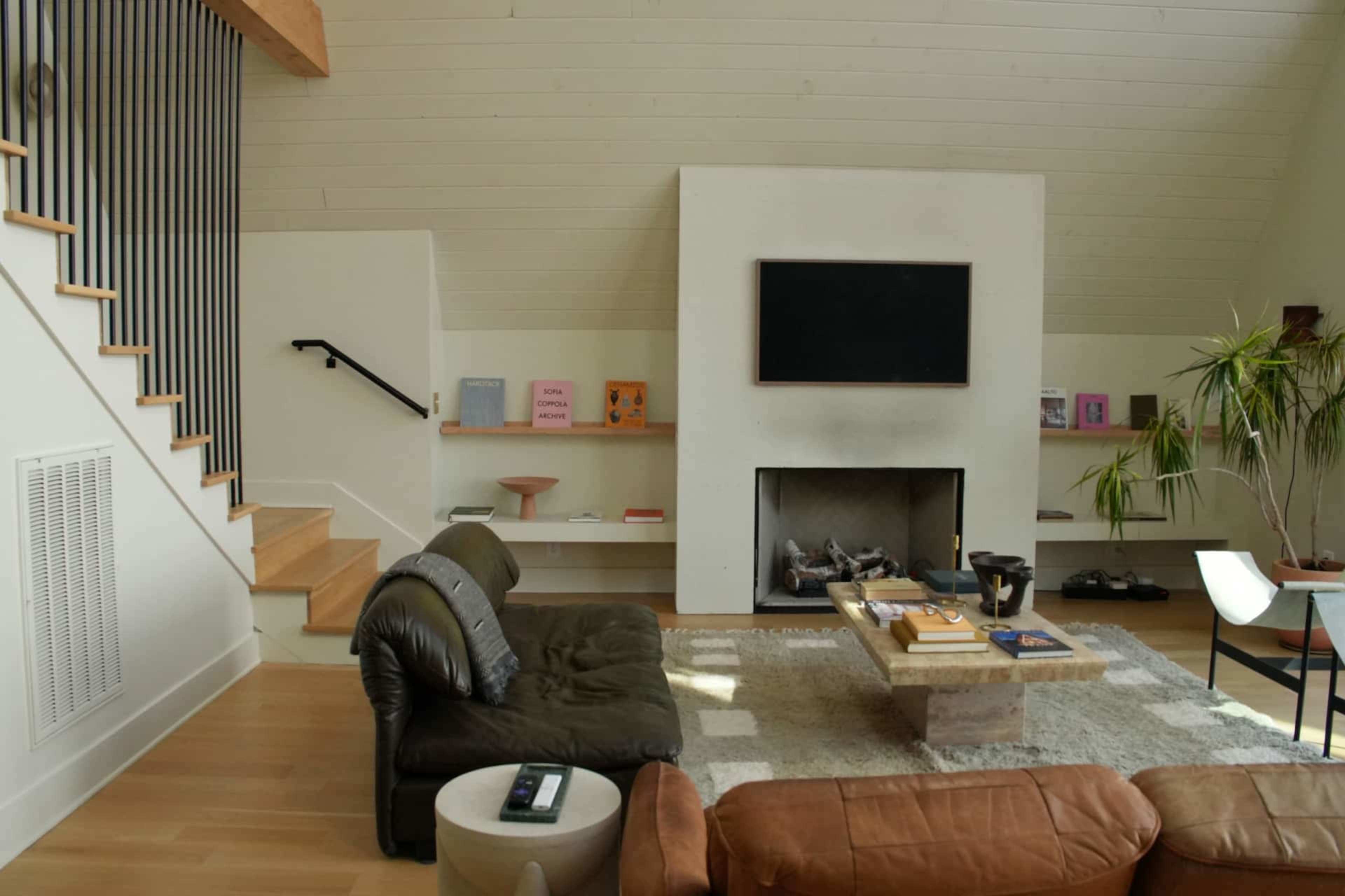 The living room features a contemporary design with a fireplace, a large sofa, a coffee table, and a flat-screen TV mounted on the wall.