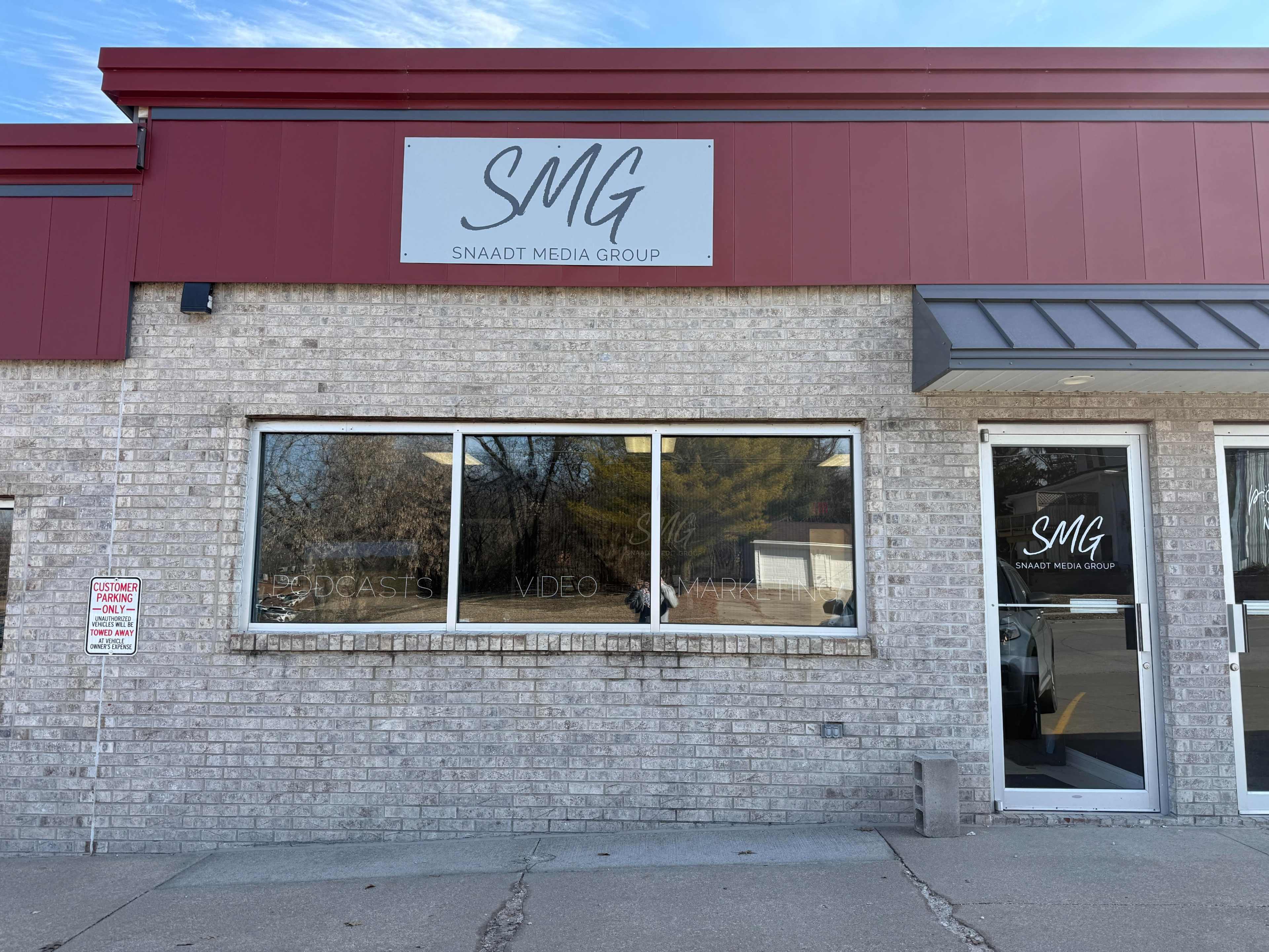 The image shows the exterior of a brick building with a red and gray facade, featuring the sign "Snaadt Media Group" and large windows.