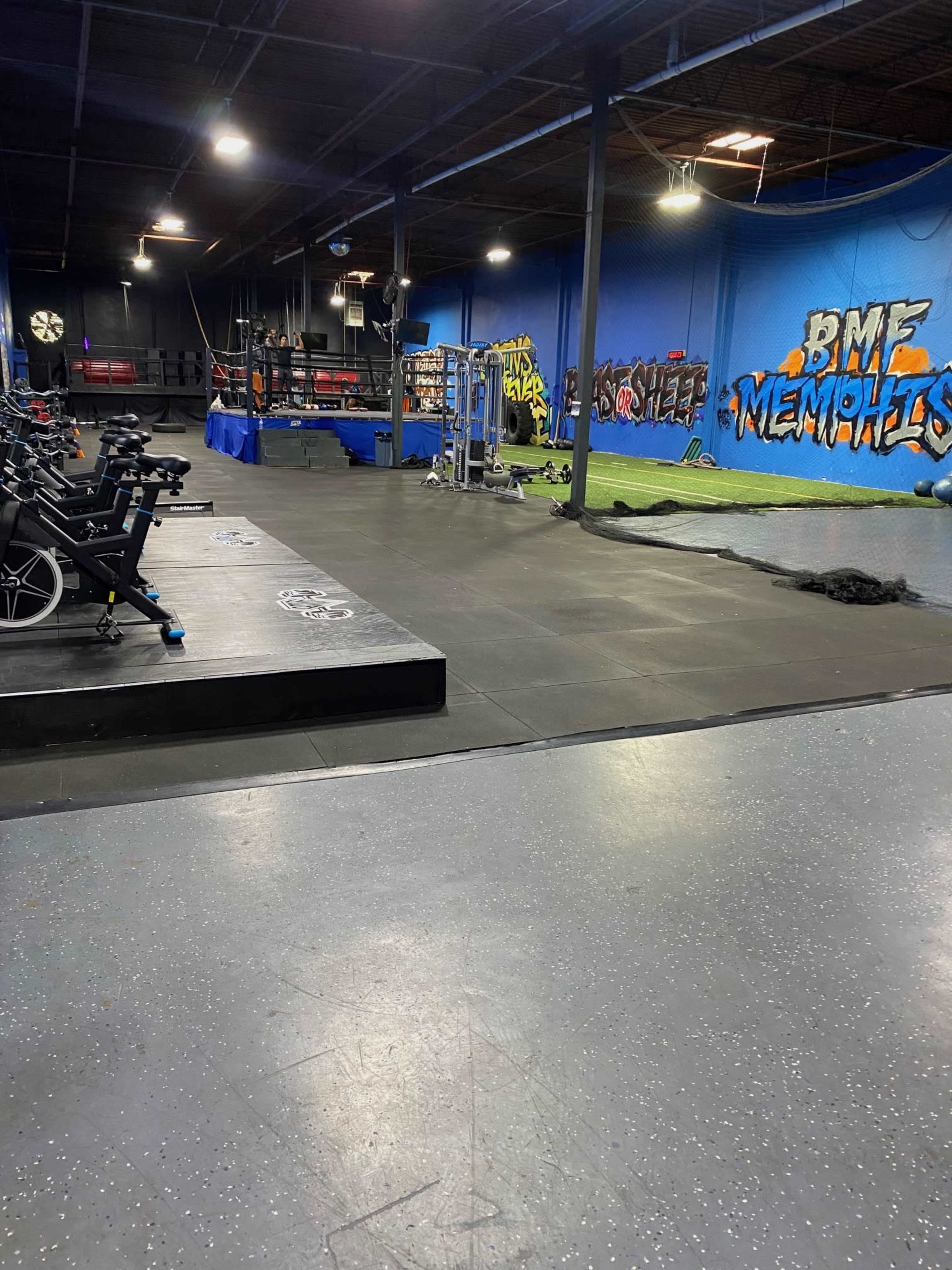 An indoor gym area featuring various exercise equipment, including stationary bikes and weightlifting stations, with a colorful mural on the wall.