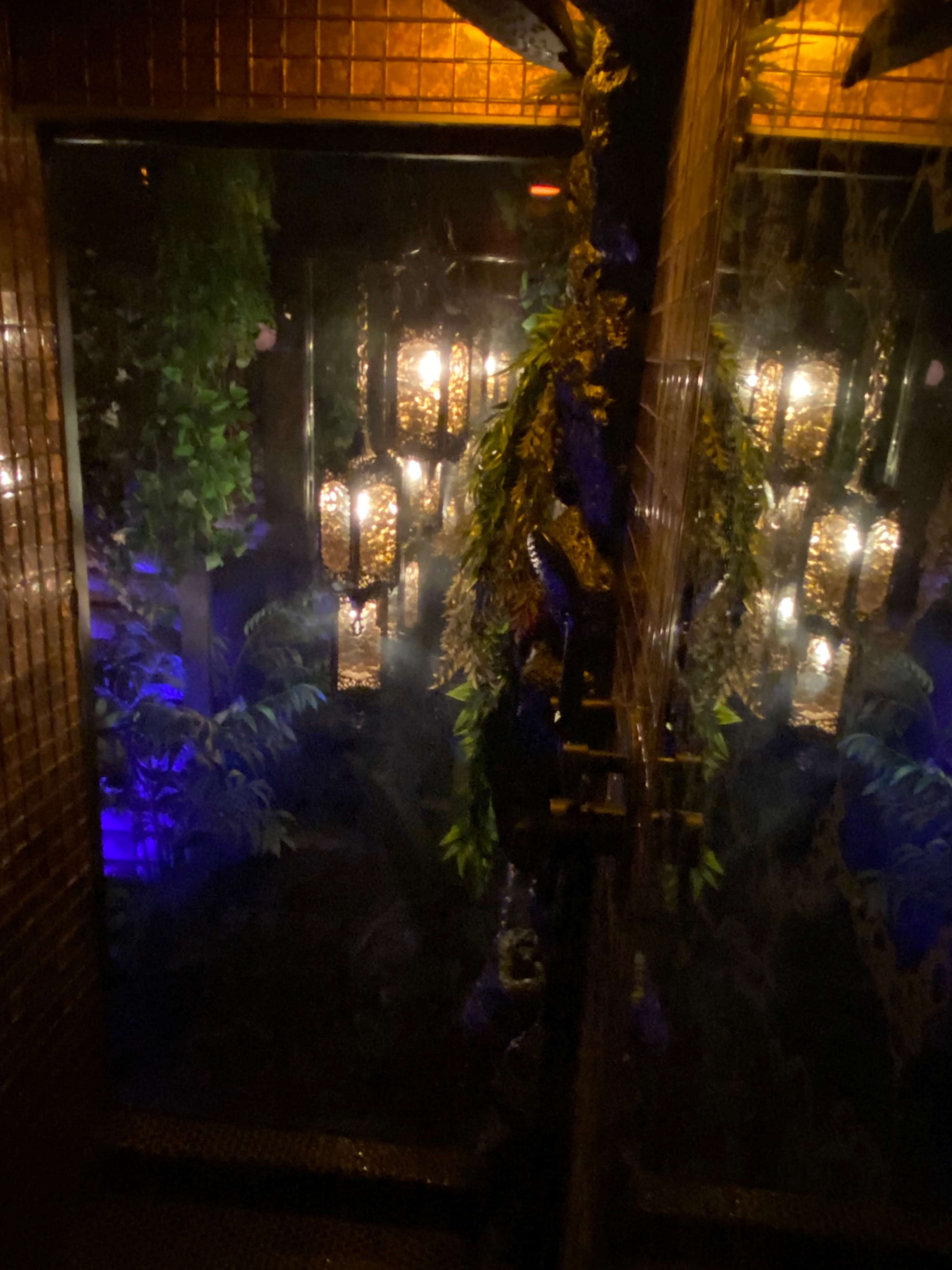 The image shows a dimly lit room with hanging lanterns surrounded by lush greenery and blue ambient lighting.