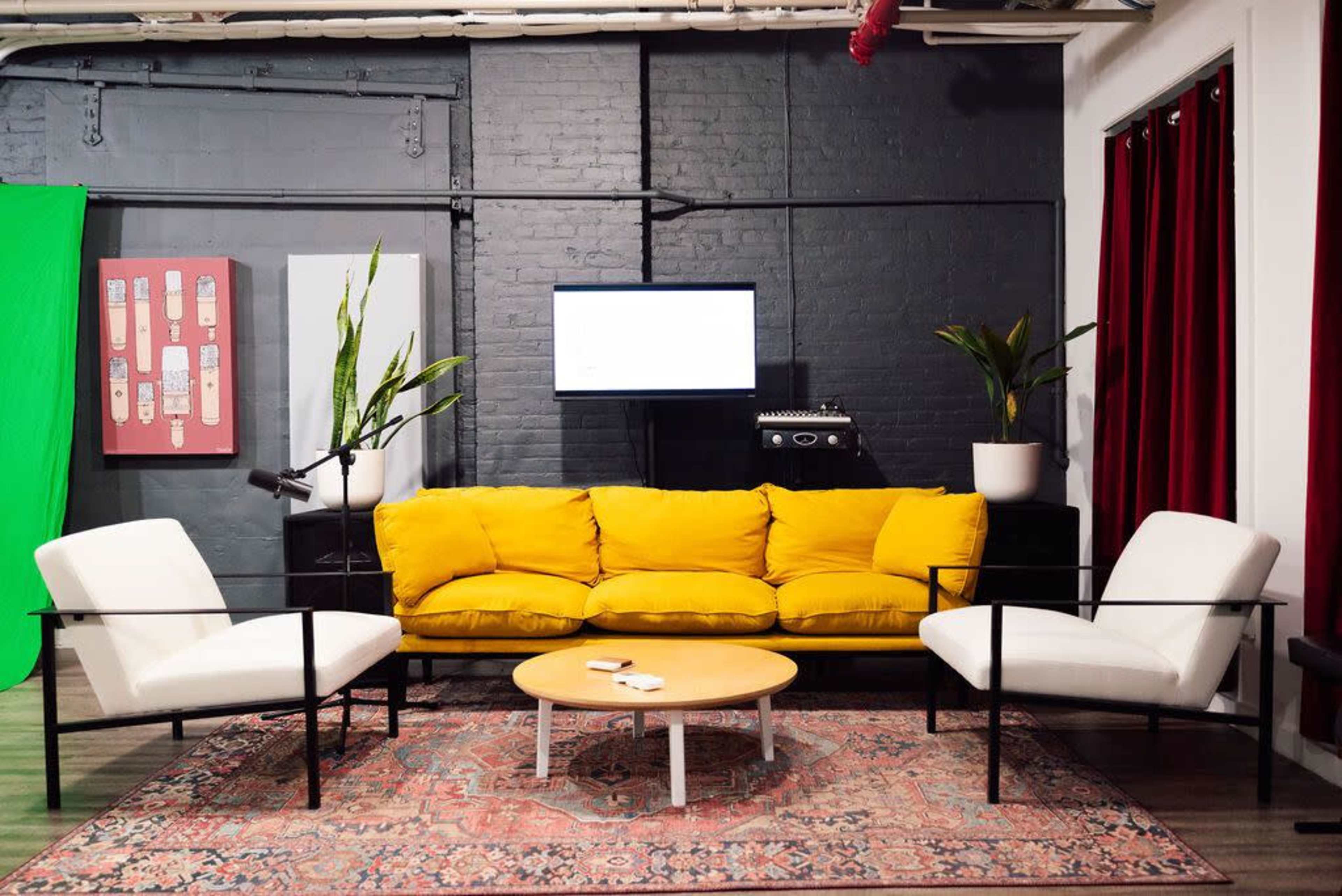 A modern living room featuring a bright yellow couch, two white armchairs, a round coffee table, and decorative plants, set against a backdrop of black brick walls and red curtains.