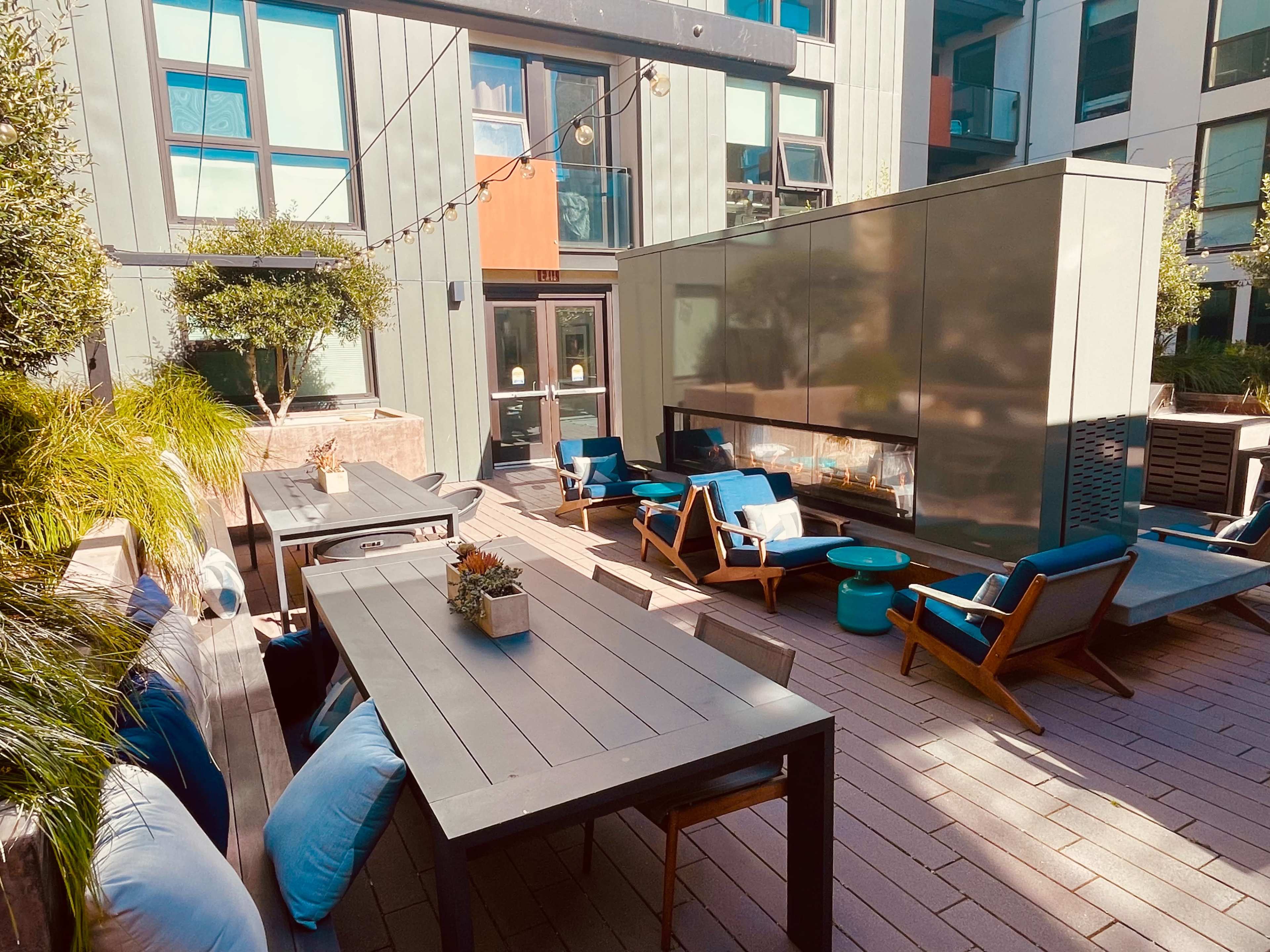 A modern outdoor patio area with seating, a fire feature, and greenery in a residential setting.