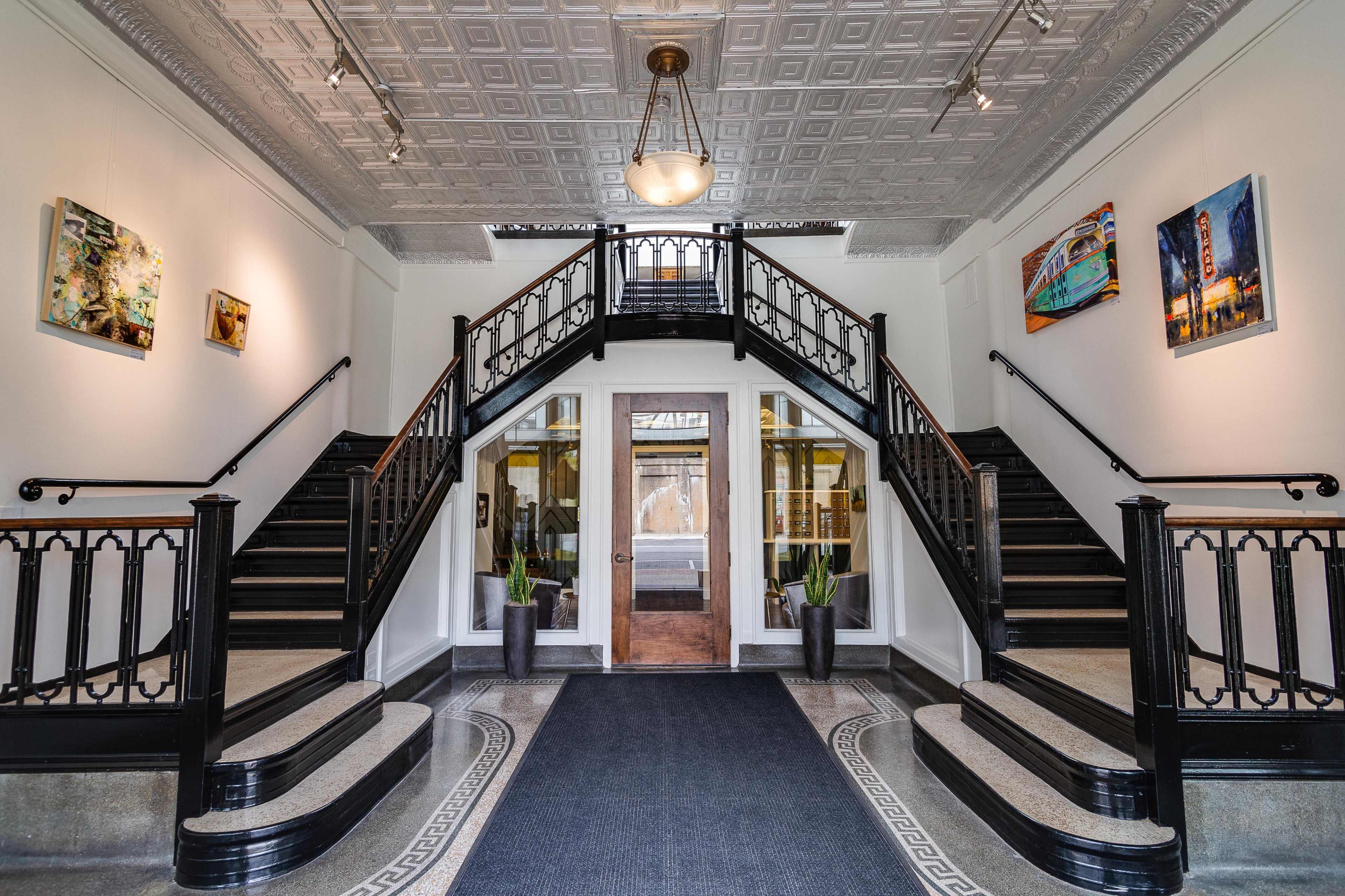 A grand entrance hall with a double staircase leading to an upper level, framed by decorative wall art and large windows.