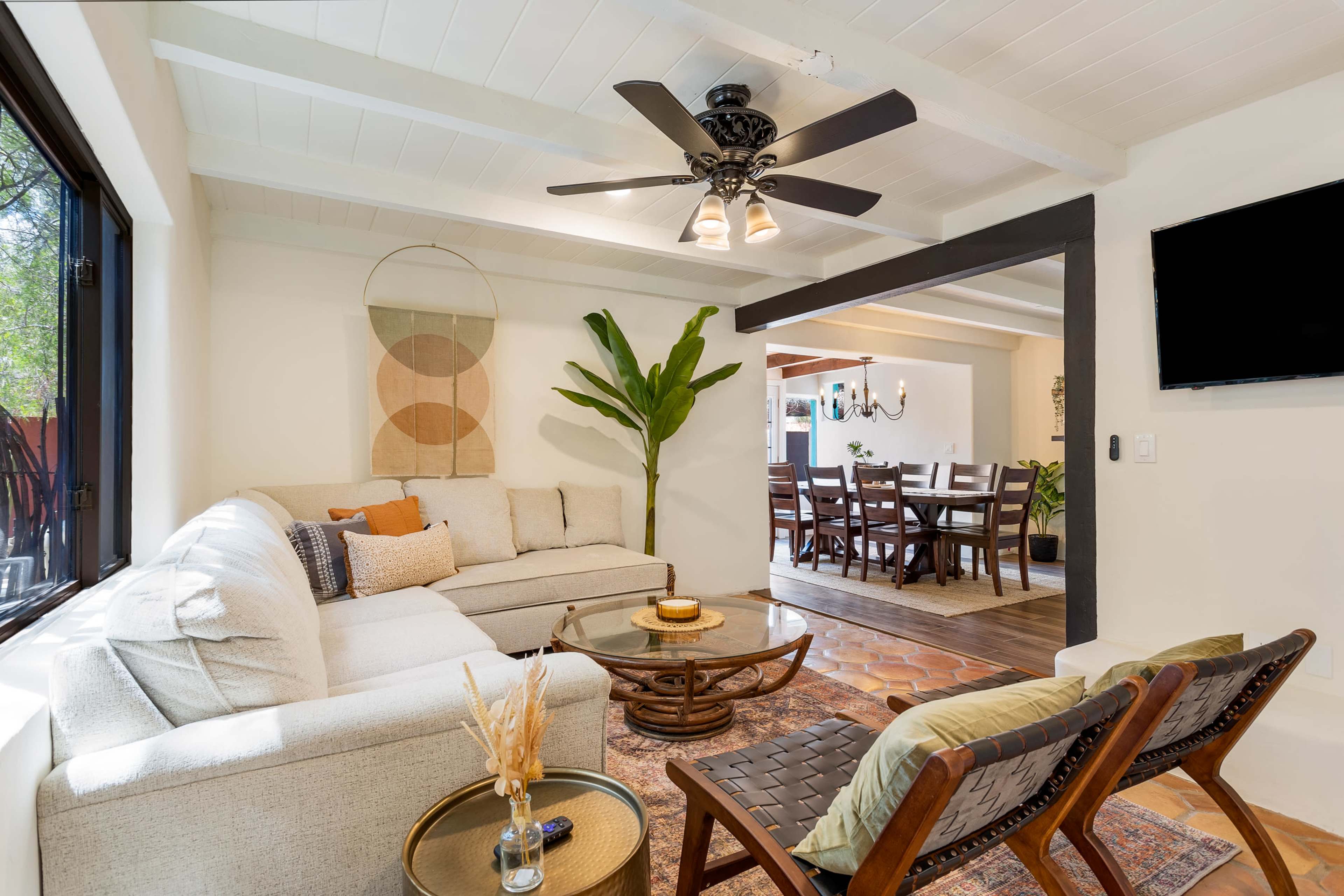 A living room featuring a sectional sofa, a coffee table, two chairs, and a ceiling fan, with an adjacent dining area visible in the background.