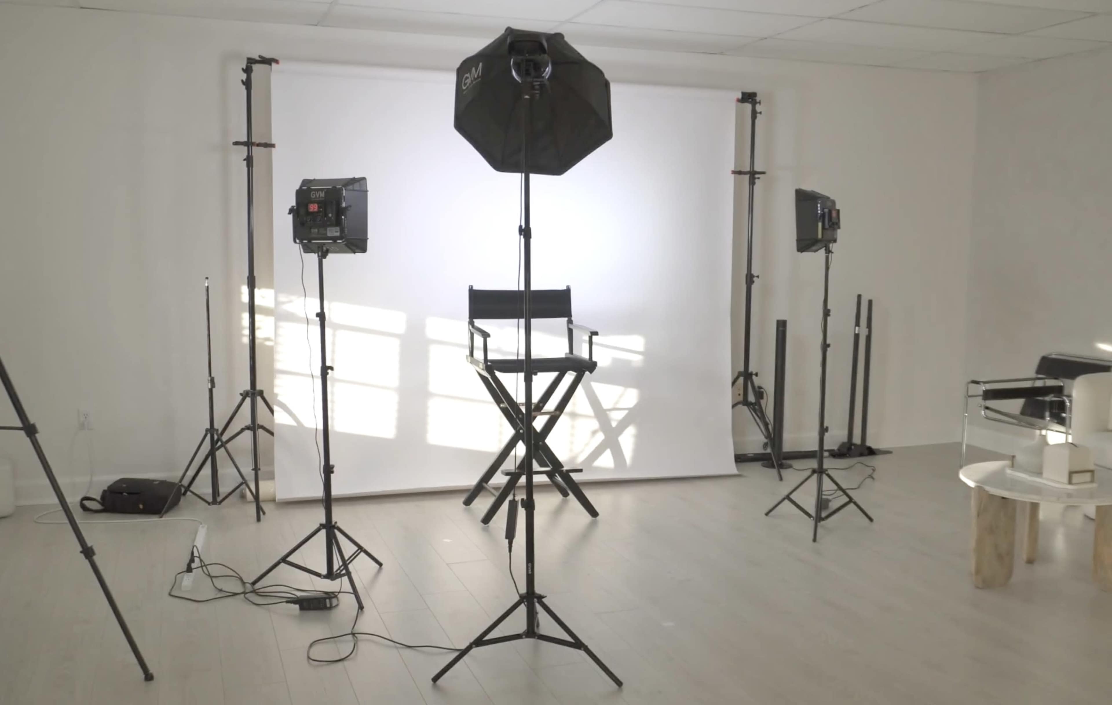 A photography studio is set up with a backdrop, a director's chair, and several lighting equipment stands.