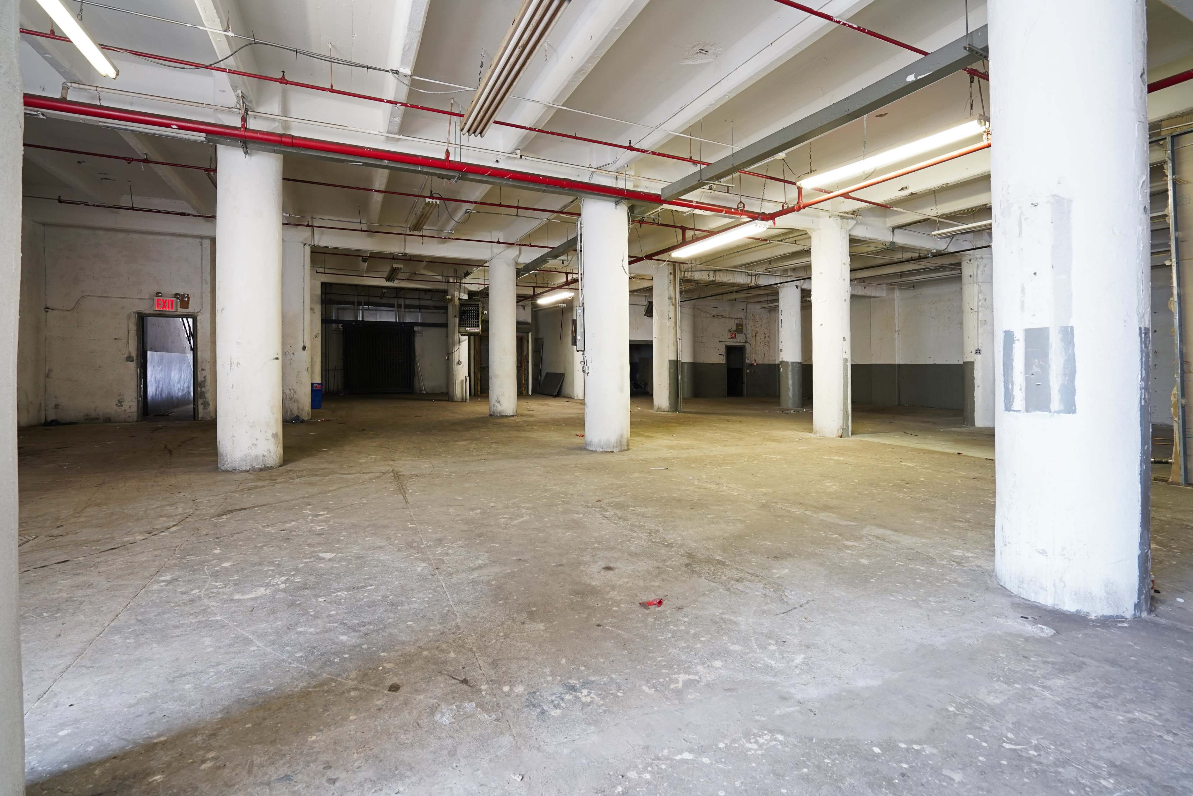 The image shows a large, empty warehouse space with concrete floors and several support columns.