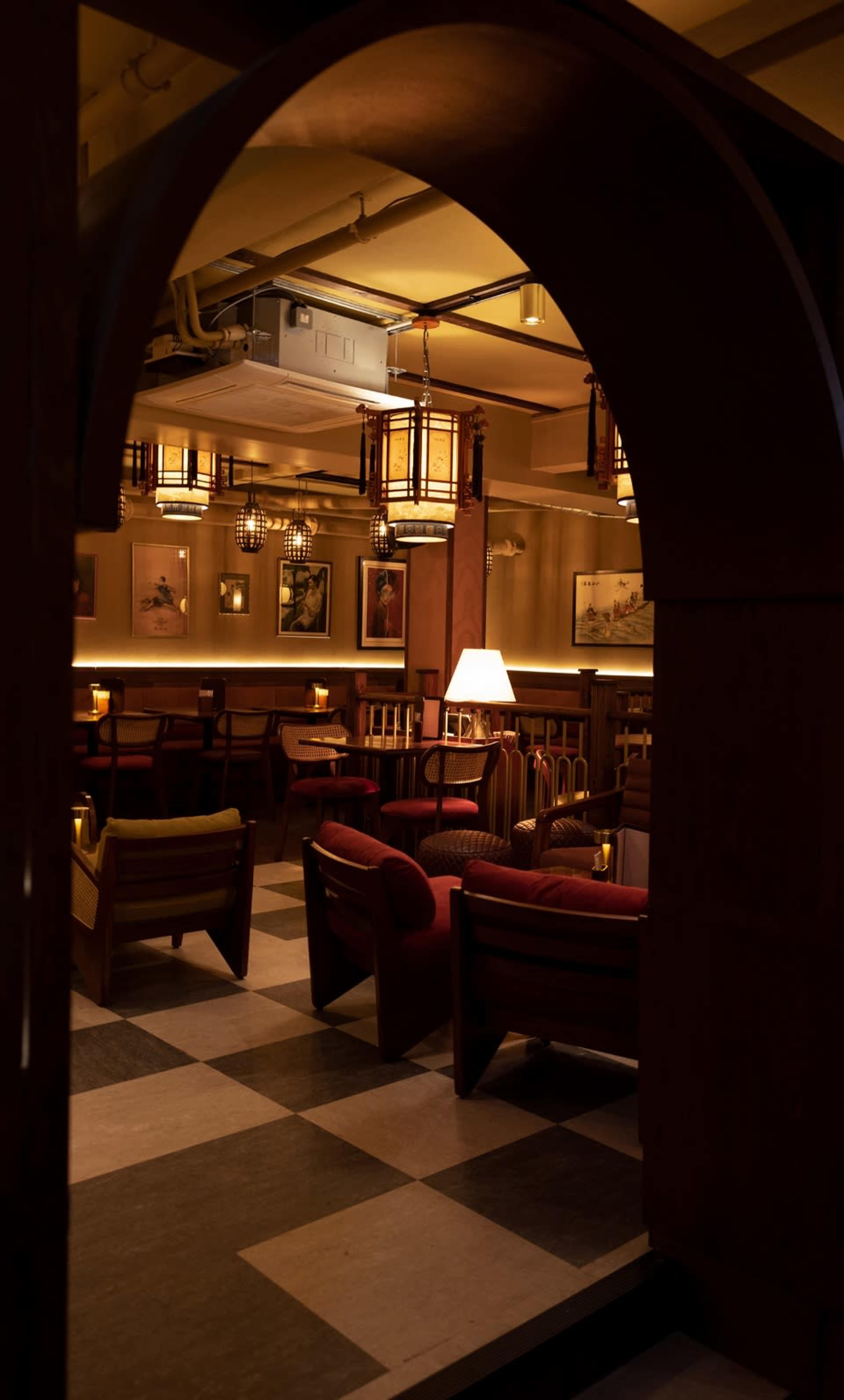 A dimly lit lounge features wooden furniture, soft lighting, and checkered flooring, creating a cozy atmosphere.