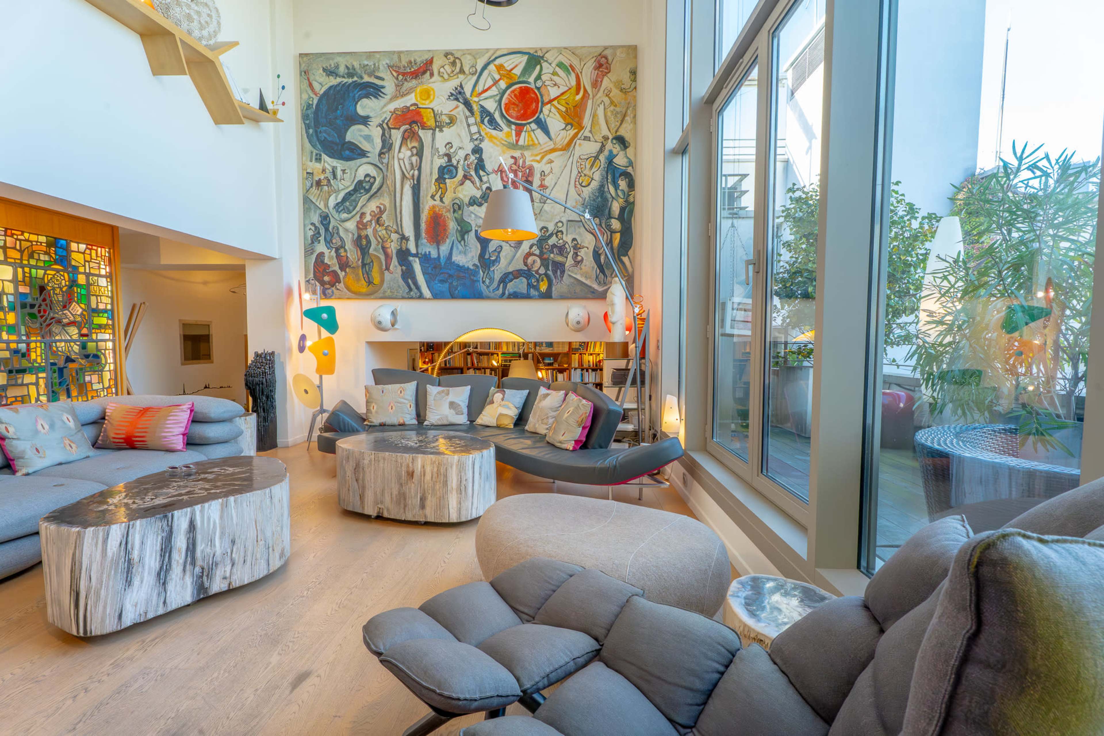 The spacious living room features a large mural, modern furniture, and multiple large windows that let in natural light.