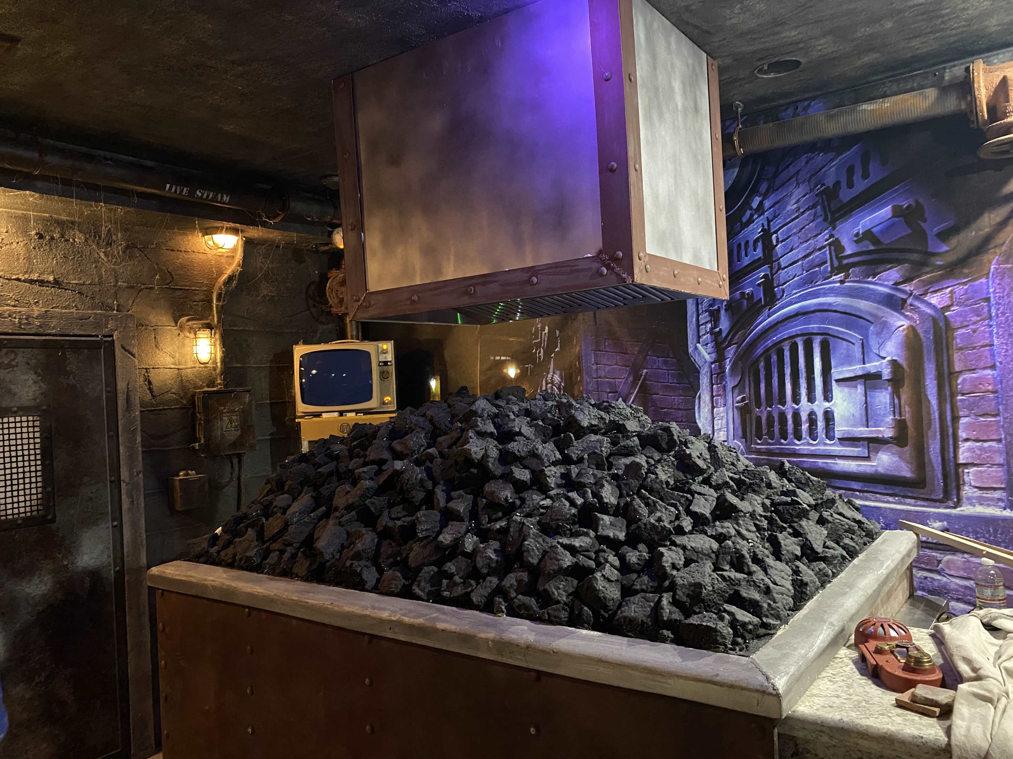A large container is suspended above a mound of black coal in a dark, industrial setting.