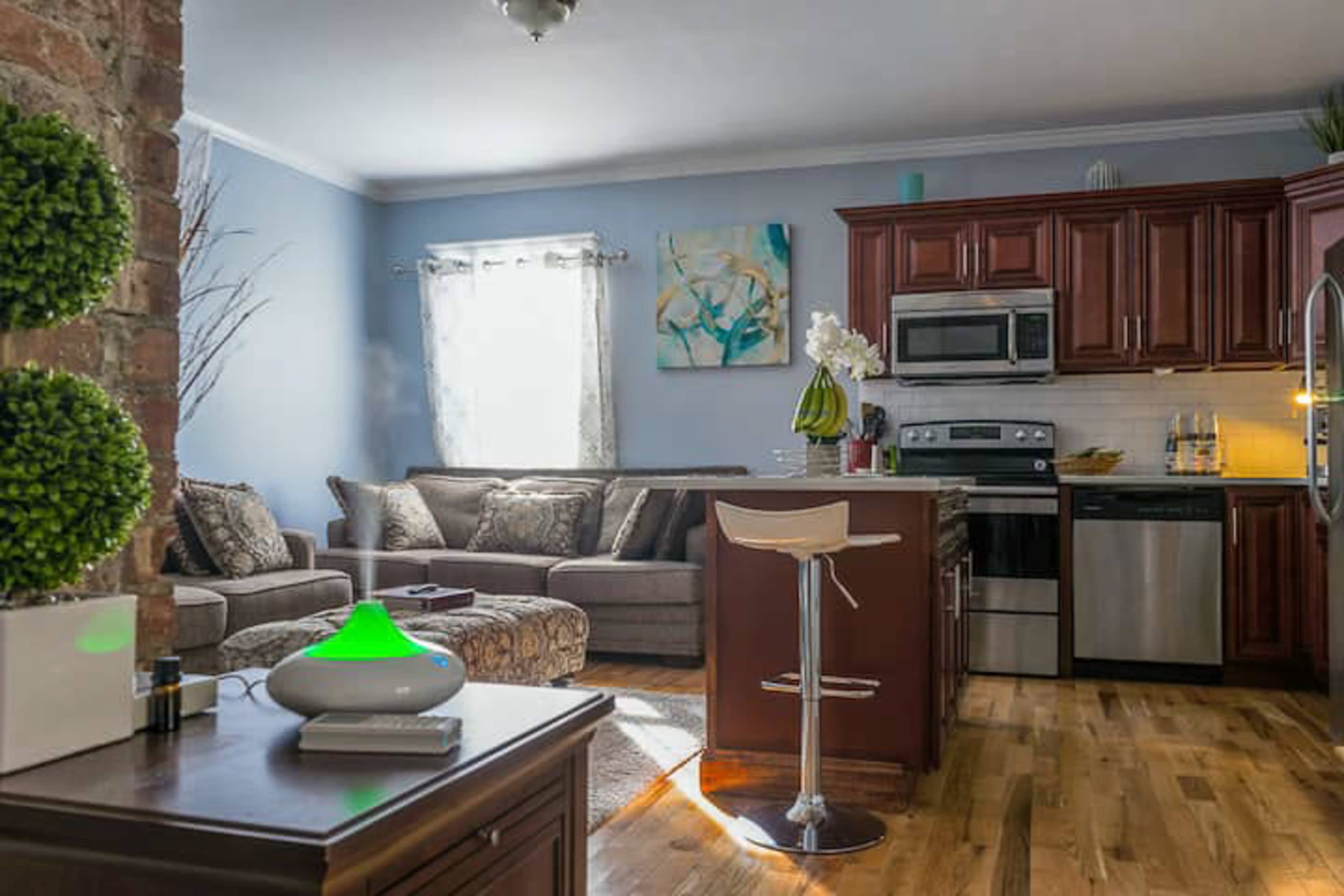 A modern living area and kitchen combination featuring a comfortable sofa, a kitchen island with bar stools, and wooden flooring.