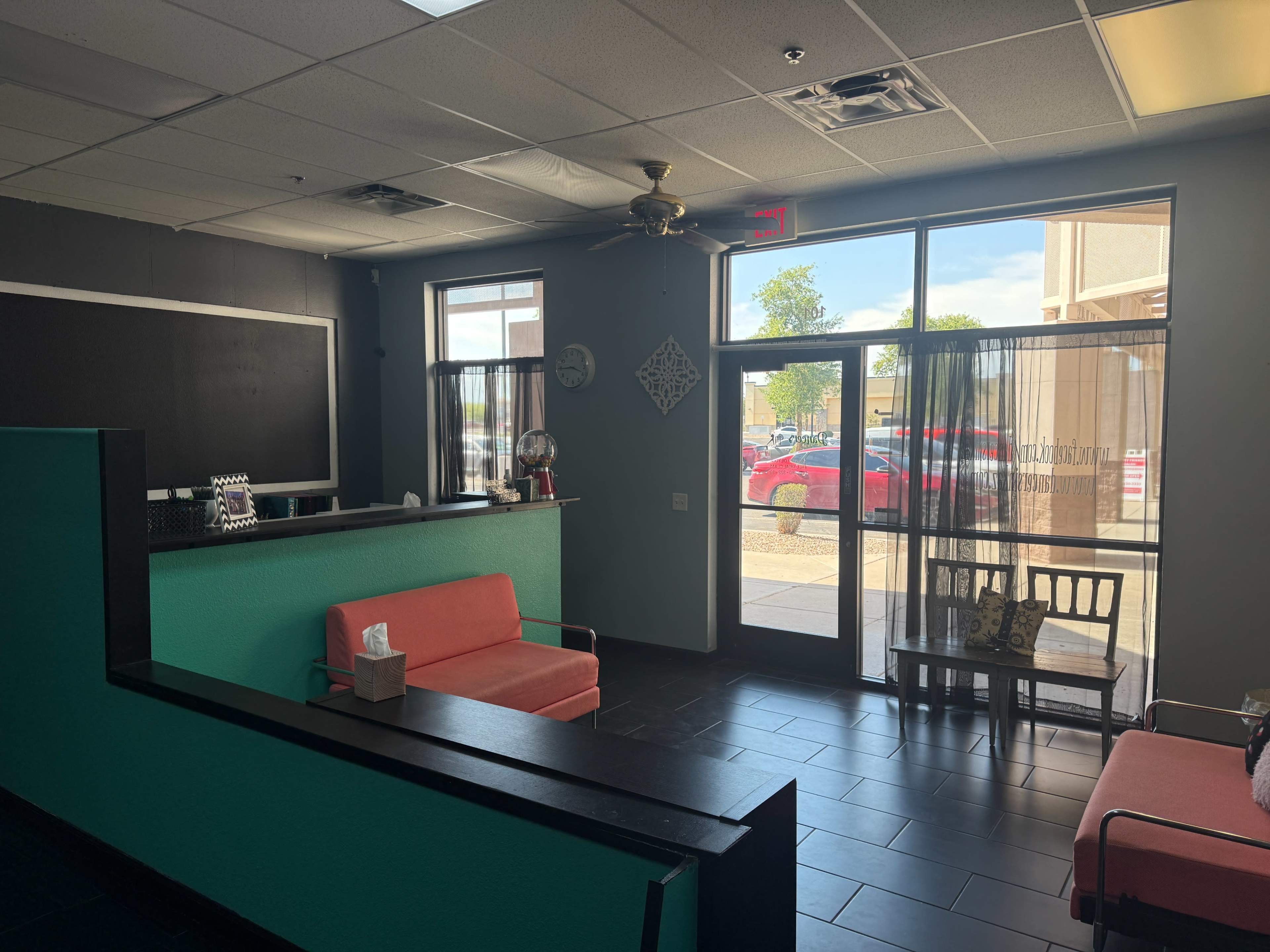 The image shows a modern waiting area with a couple of orange couches, a black reception desk, and large windows allowing natural light to enter.