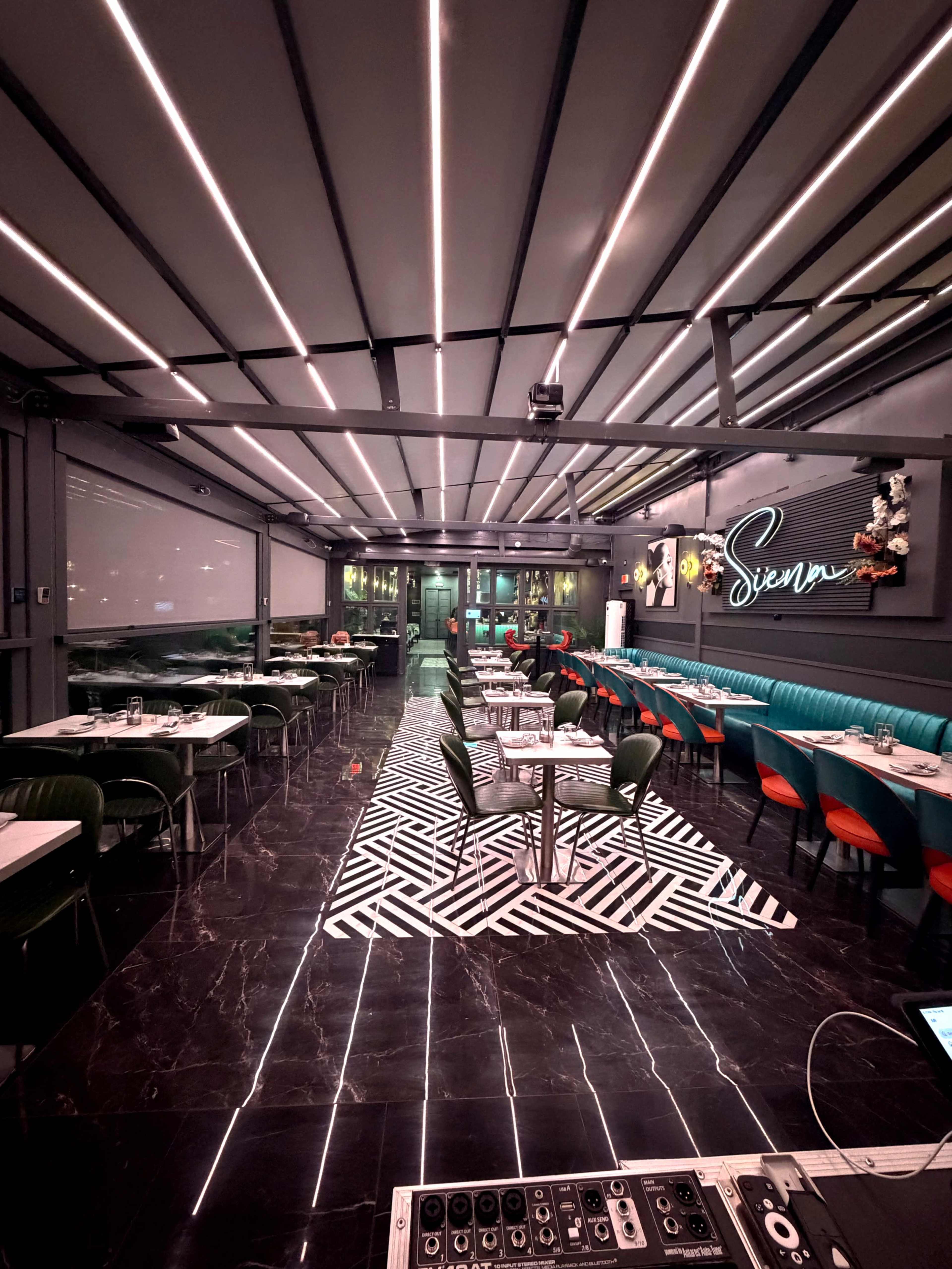 The image shows a modern restaurant interior with patterned flooring, green and red seating, and vibrant lighting.