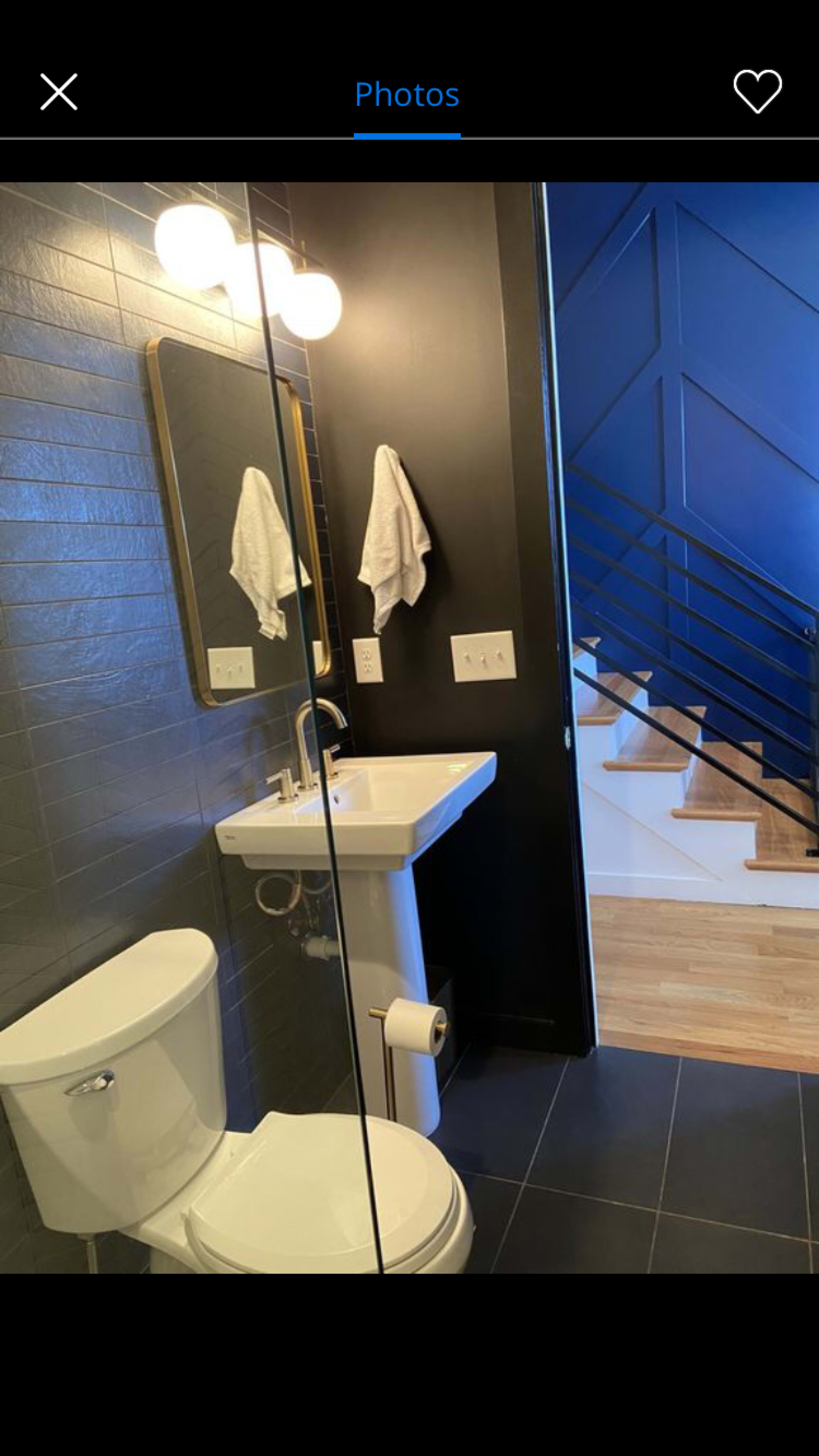 A modern bathroom with a toilet, sink, and mirror, adjacent to a staircase with a dark blue wall.
